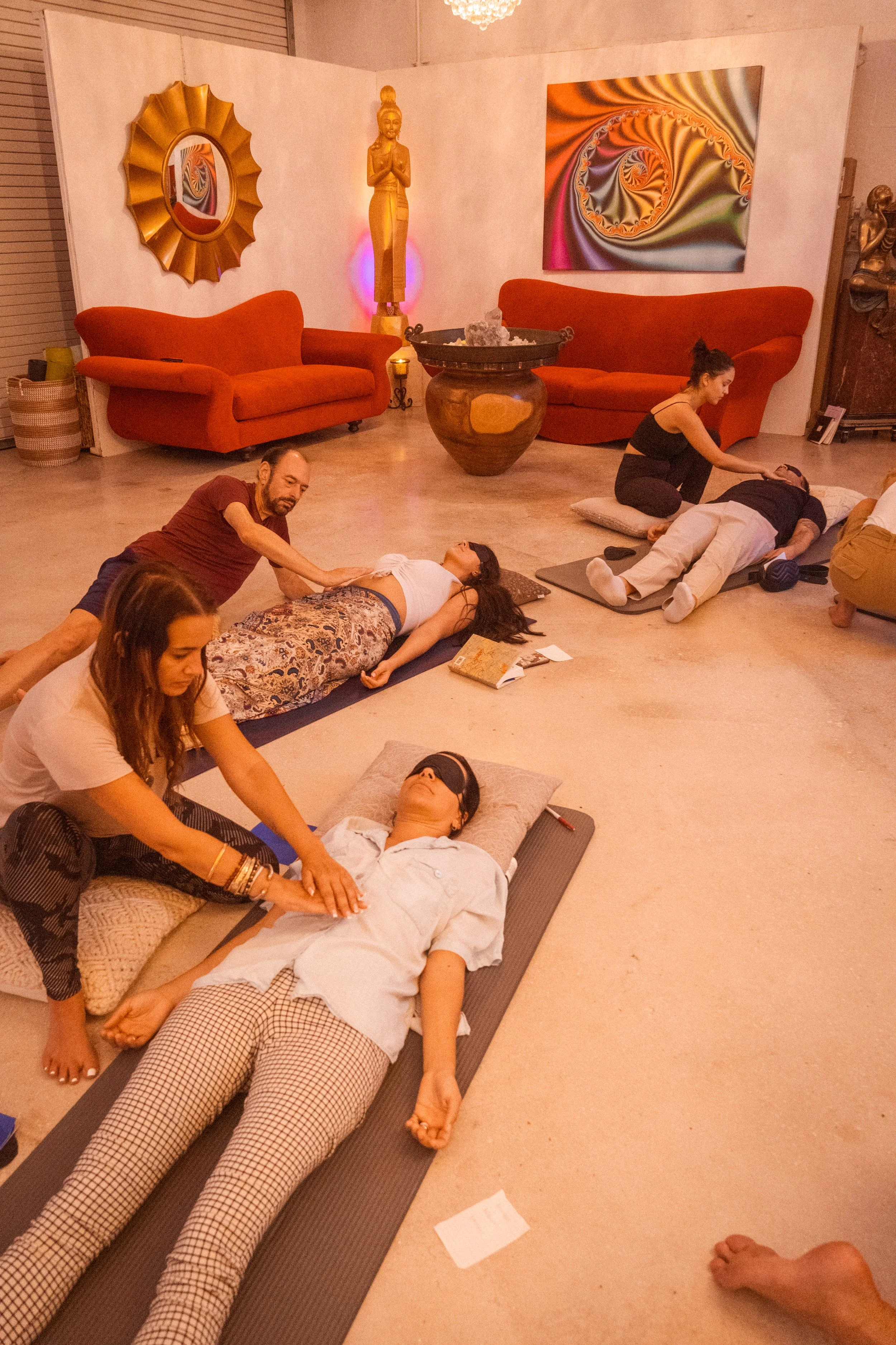 People participating in a meditation or relaxation session in a cozy room with orange couches, modern art, and sculptures.