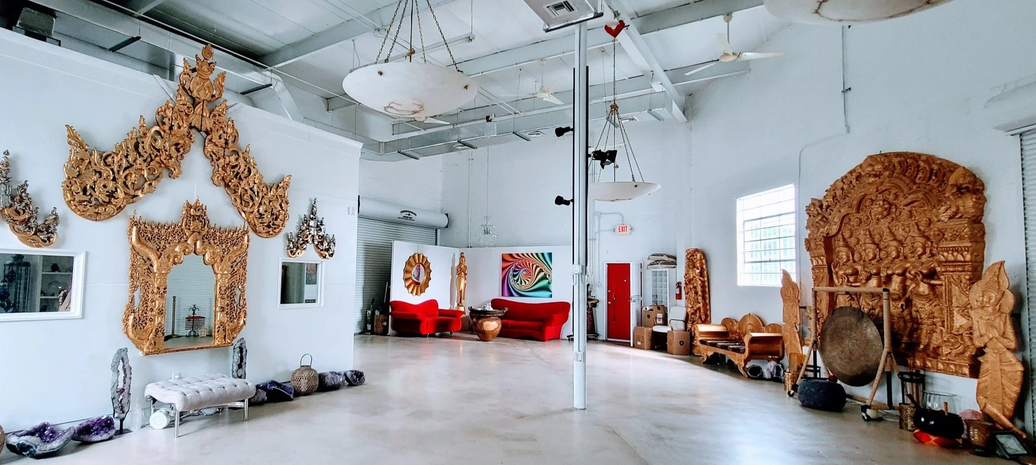 Interior of a room decorated with ornate wooden carvings, red sofas, and various decorative objects, with a high ceiling and large windows.