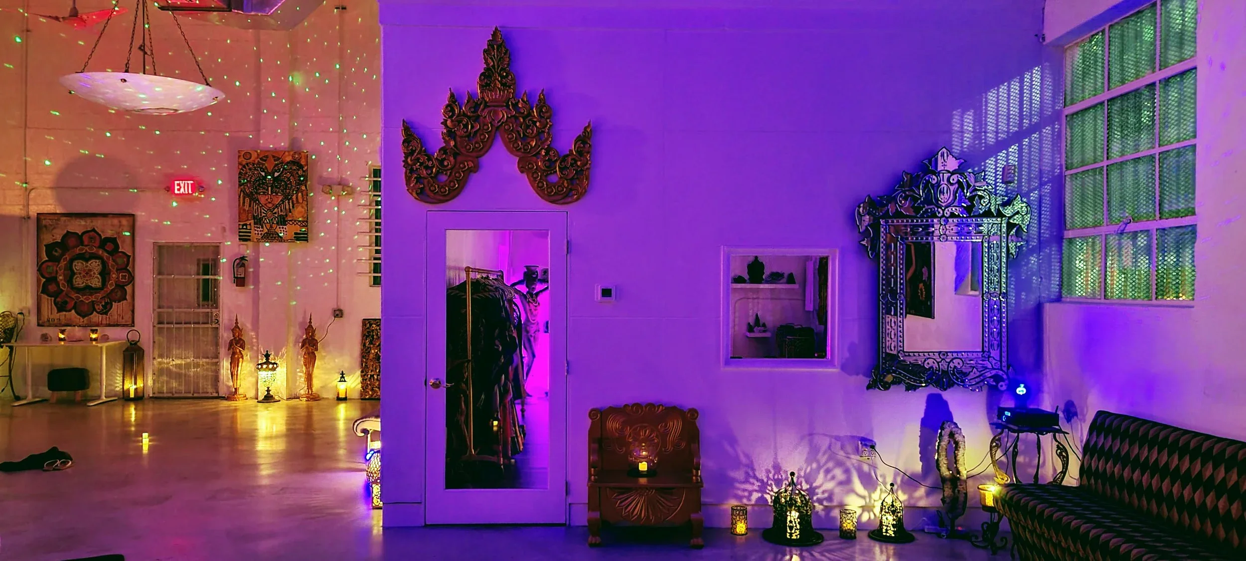 Interior of a decorated room with colorful lighting, echoing a festive or cultural theme, featuring art, mirrors, illuminated lanterns, and a patterned sofa.