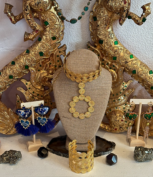 Display of gold jewelry including a necklace, earrings, and a bracelet, with decorative elephant sculptures in the background.