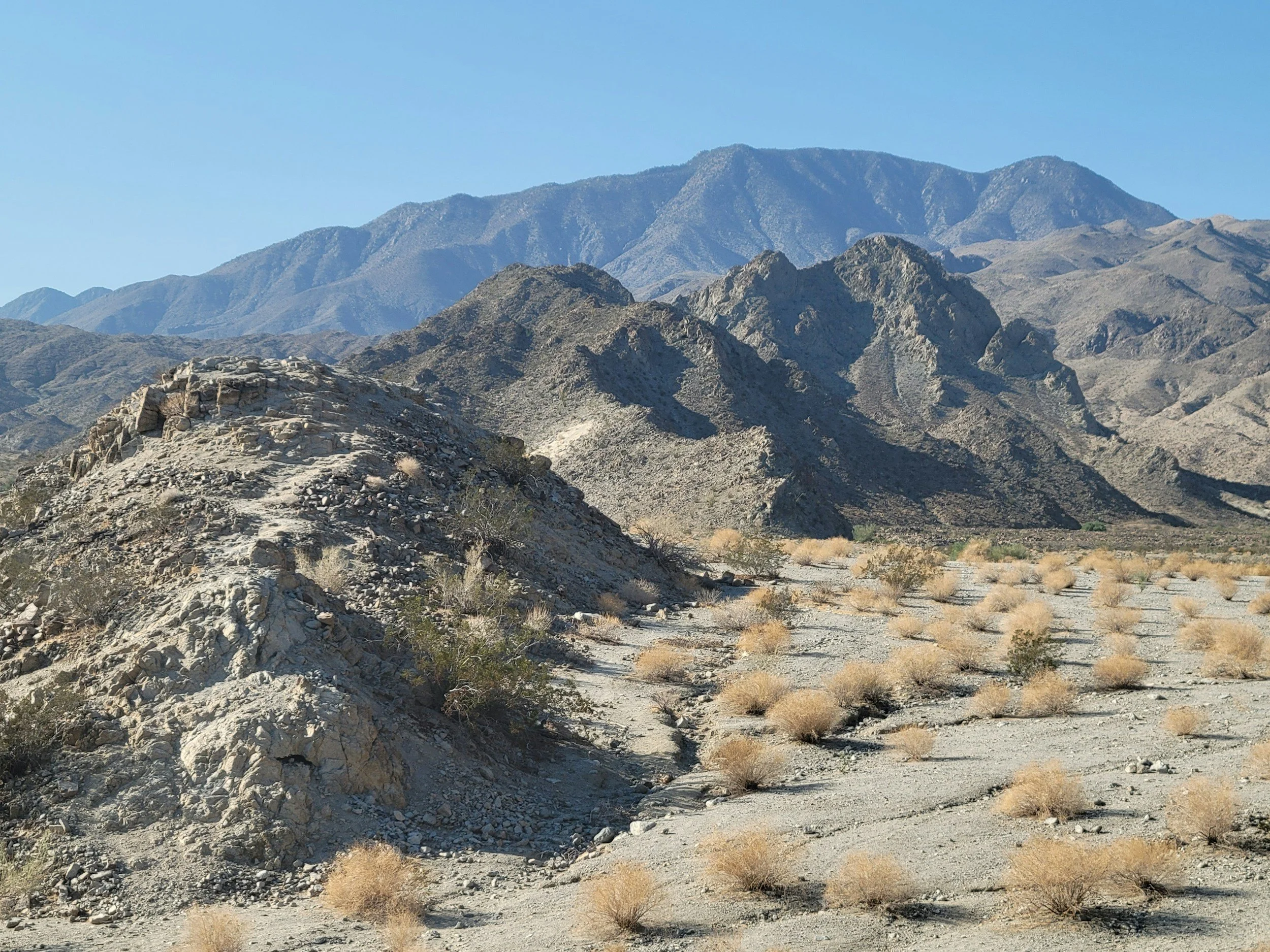 Desert landscape with rocky hills and sparse desert shrubs under a clear blue sky.