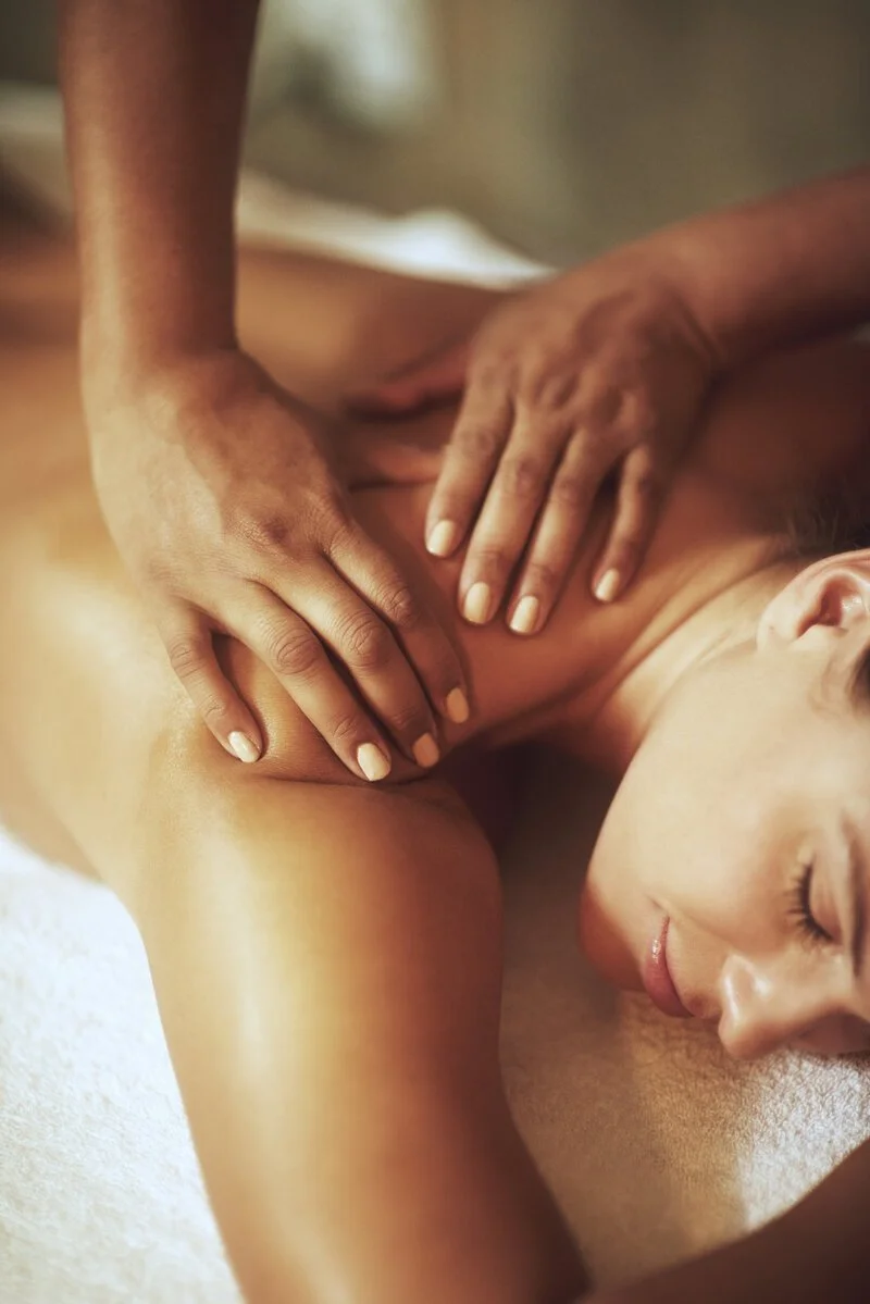 A woman receiving a massage, lying on her side with eyes closed and a relaxed expression.