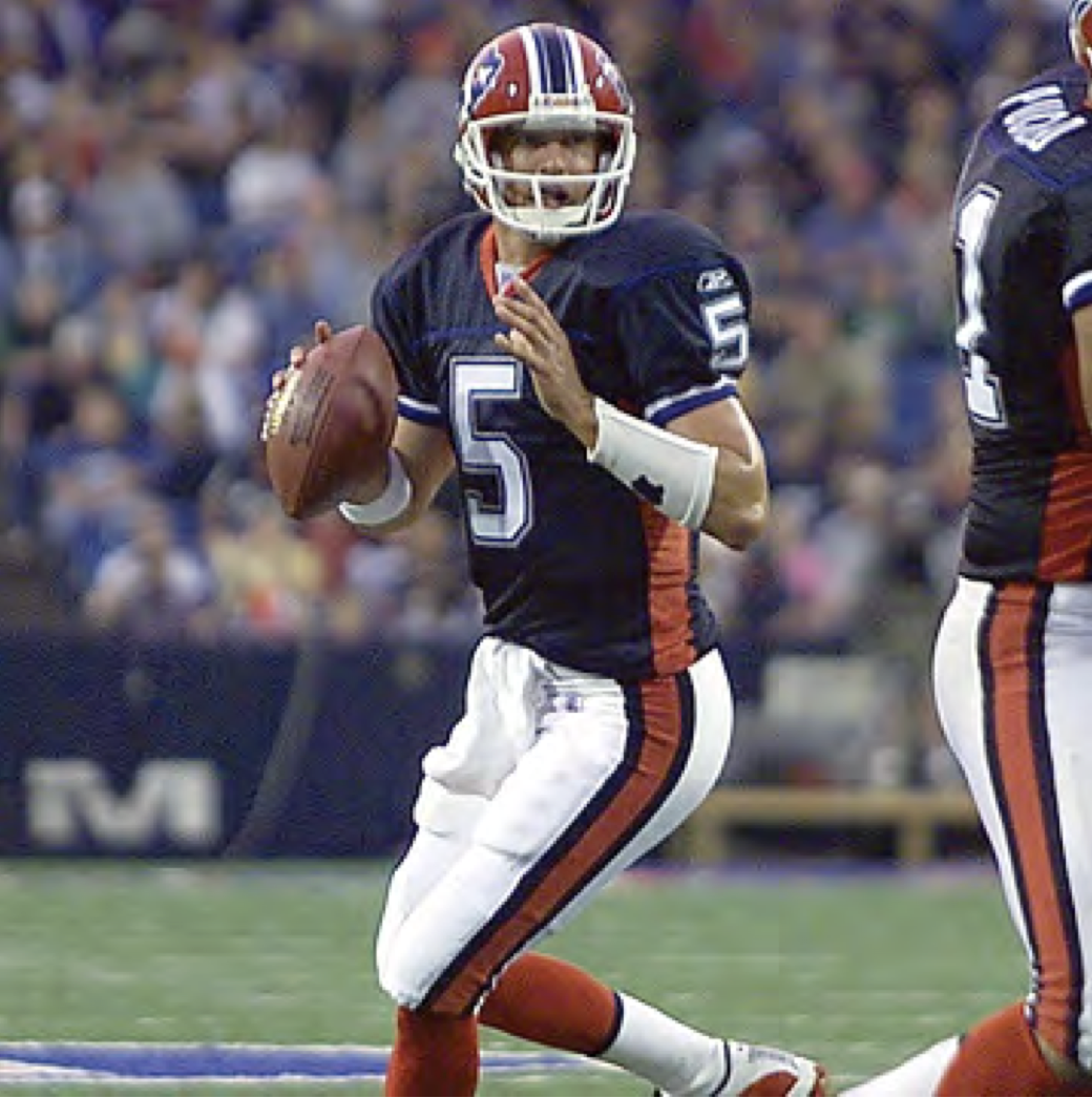A football player wearing the number 5 jersey, black and orange uniform, holding a football, on a football field during a game.