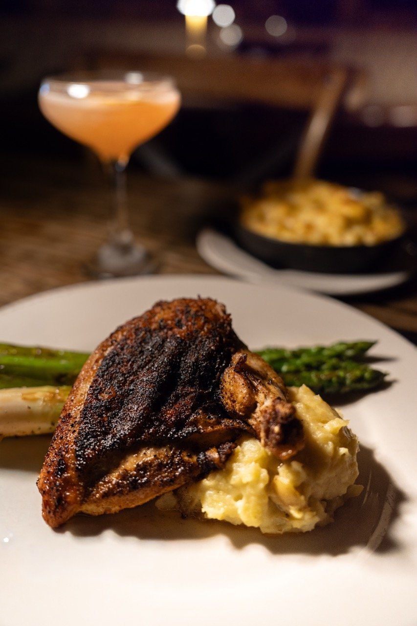 A plate with a grilled chicken thigh, mashed potatoes, and green asparagus on a white dish.