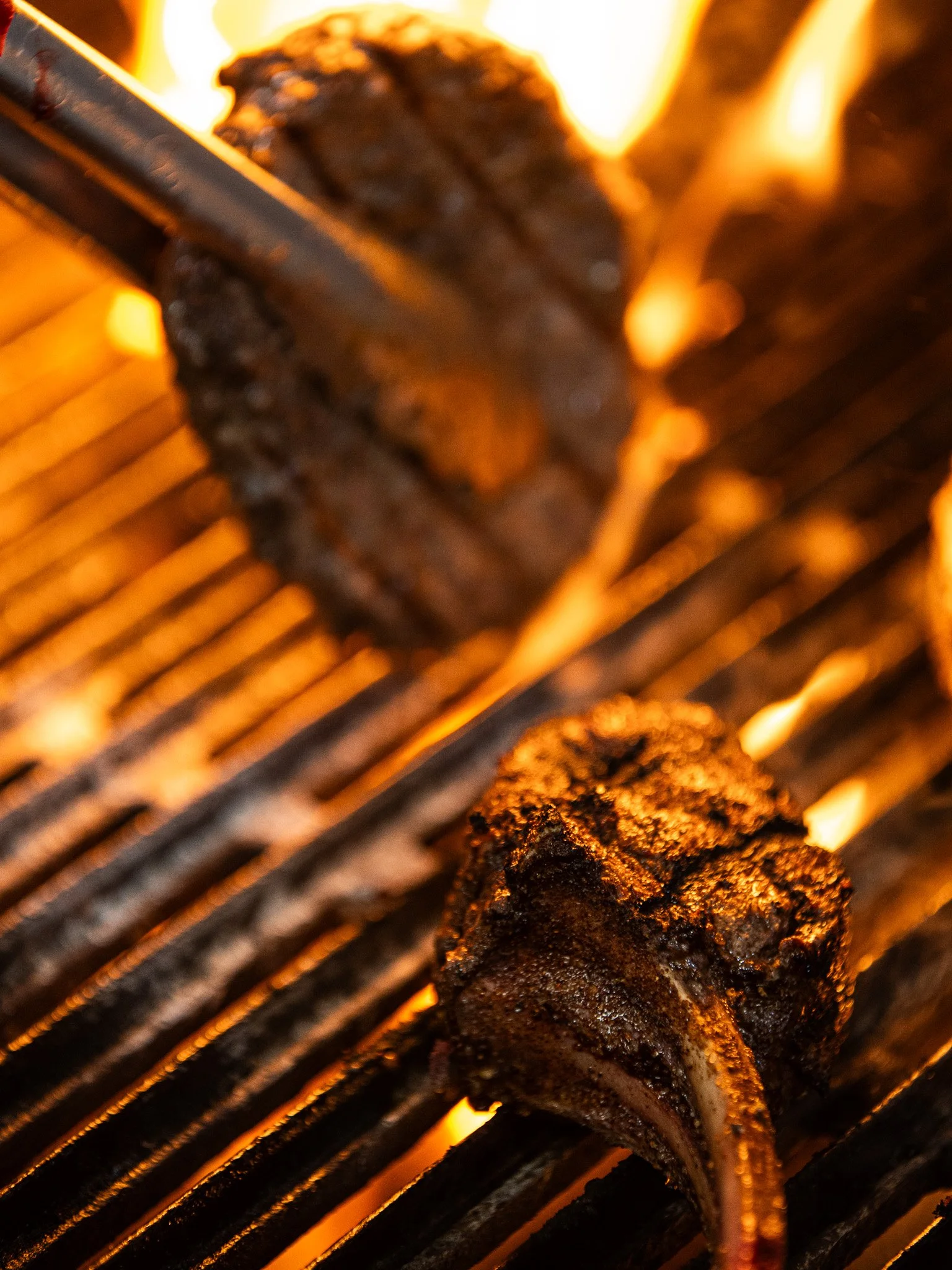 Close-up of seasoned steak and pork chop cooking on a grill over open flame.
