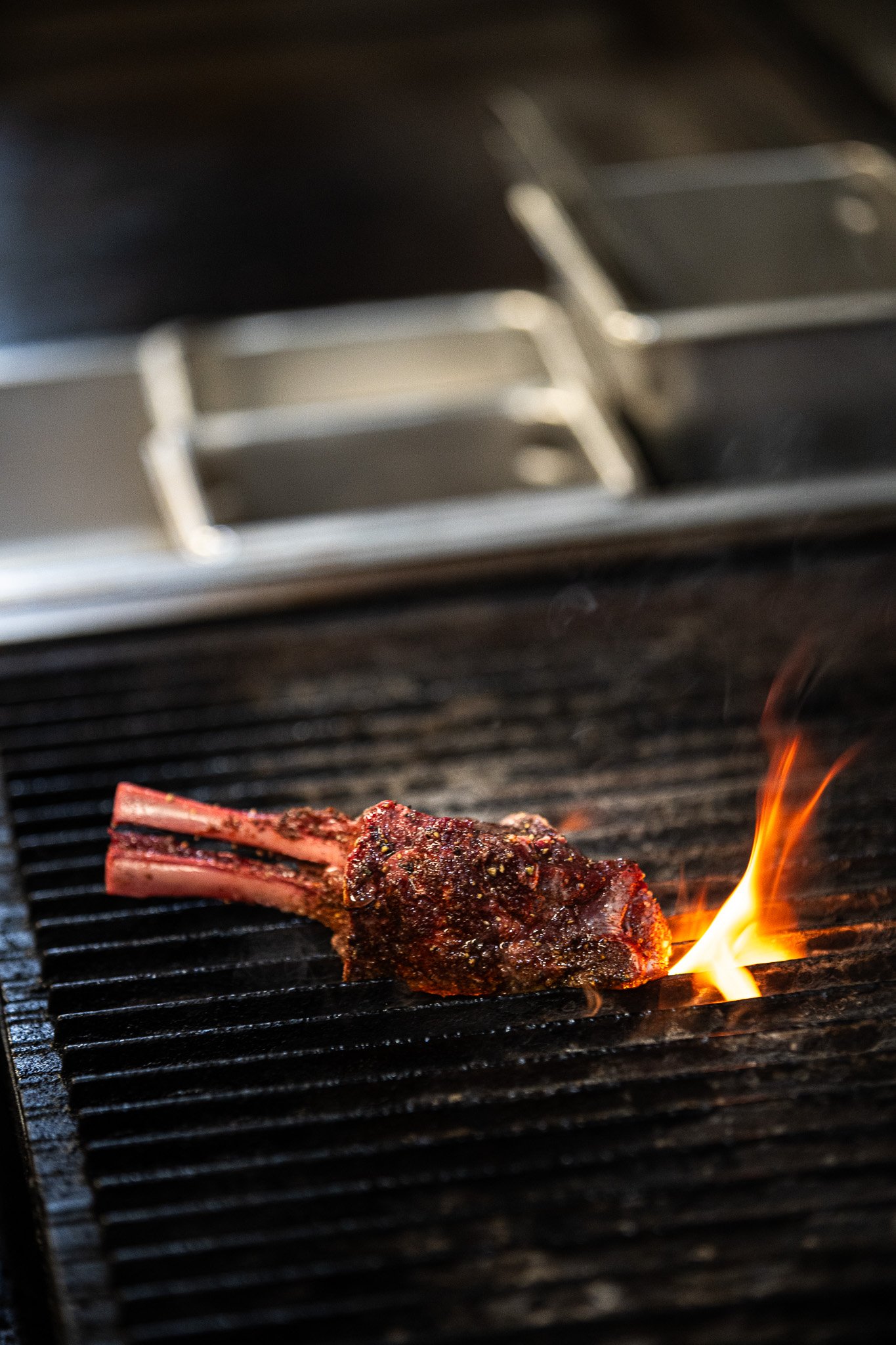 A seasoned lamb chop cooking on a grill with flames.