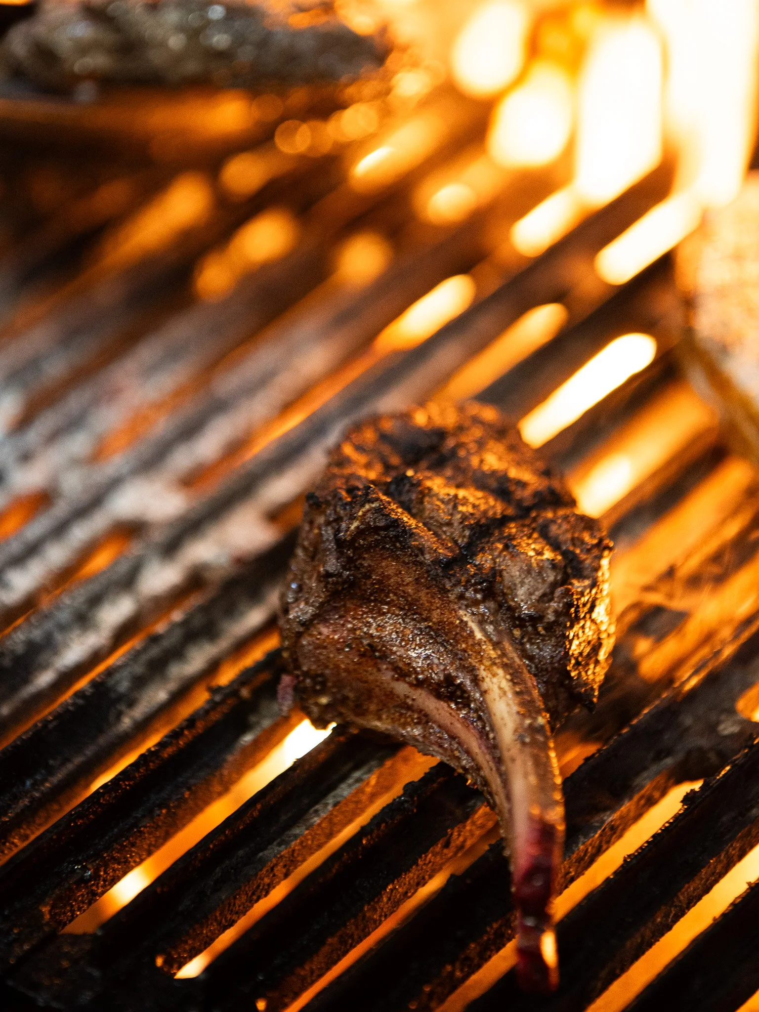 A piece of seasoned meat, possibly beef, grilling on an open flame with glowing embers