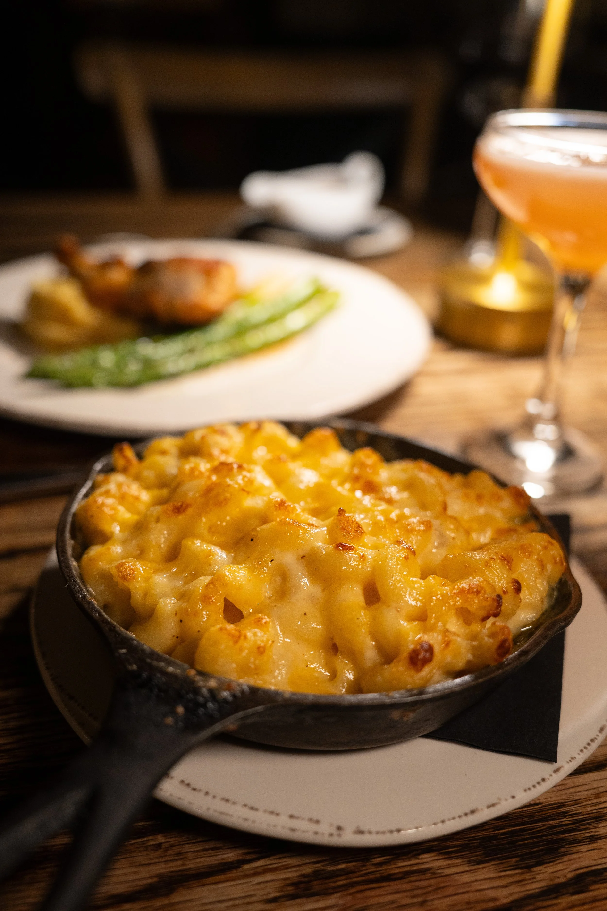 A close-up of a creamy baked macaroni and cheese in a black cast iron skillet on a white plate, placed on a wooden table.