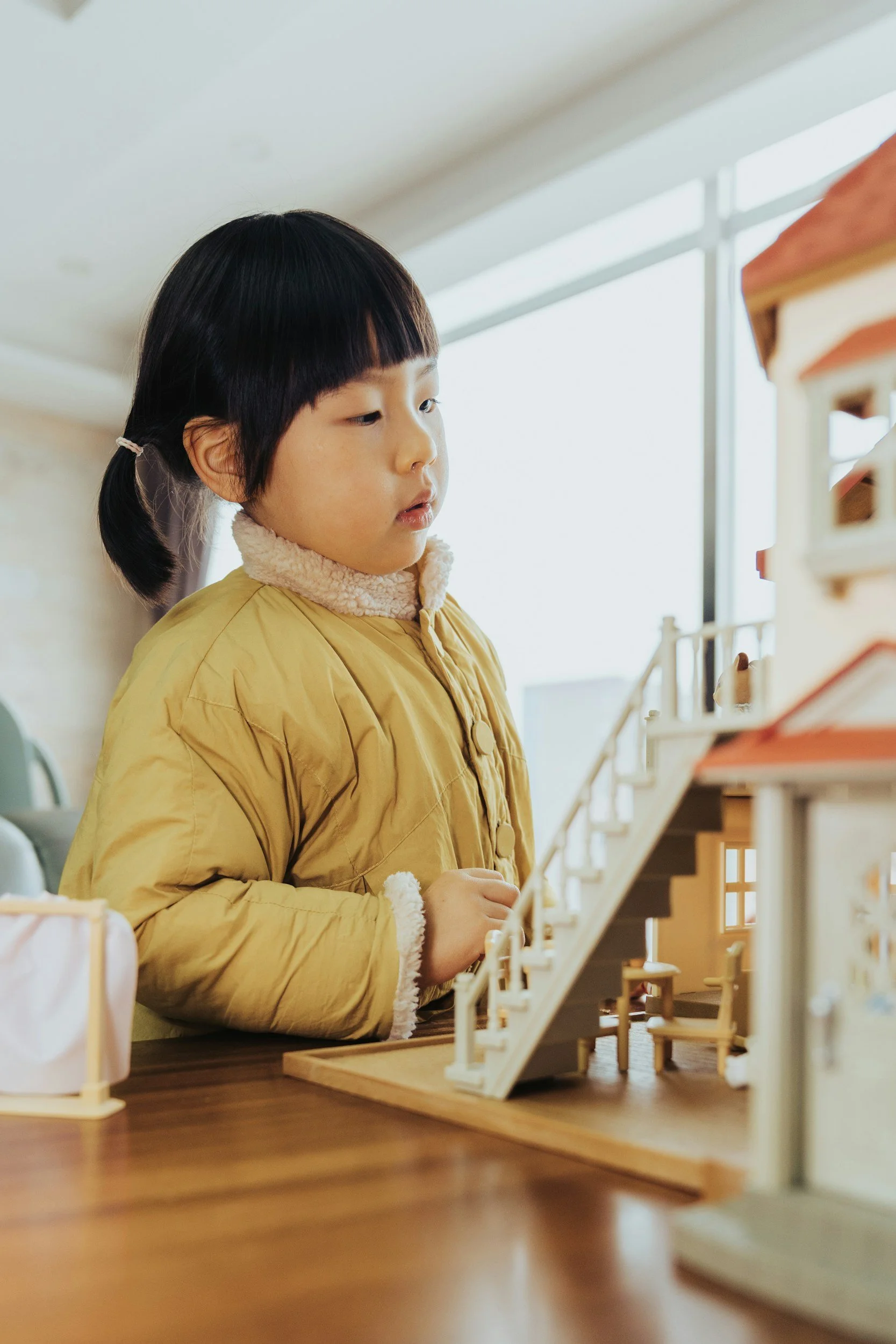 A young girl looking at a miniature dollhouse indoors.