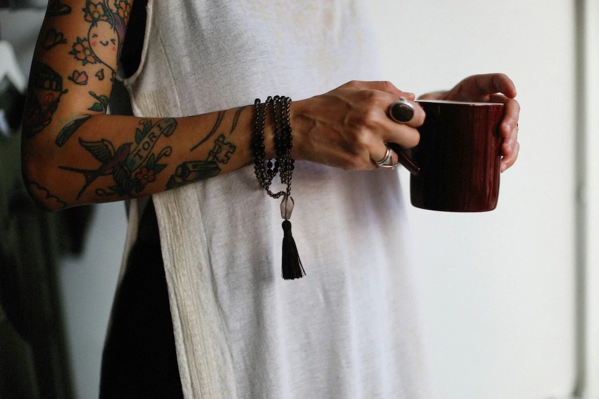 A person with tattoos holding a warm mug, illustrating the process of managing overwhelming emotions through therapy in Norwich.