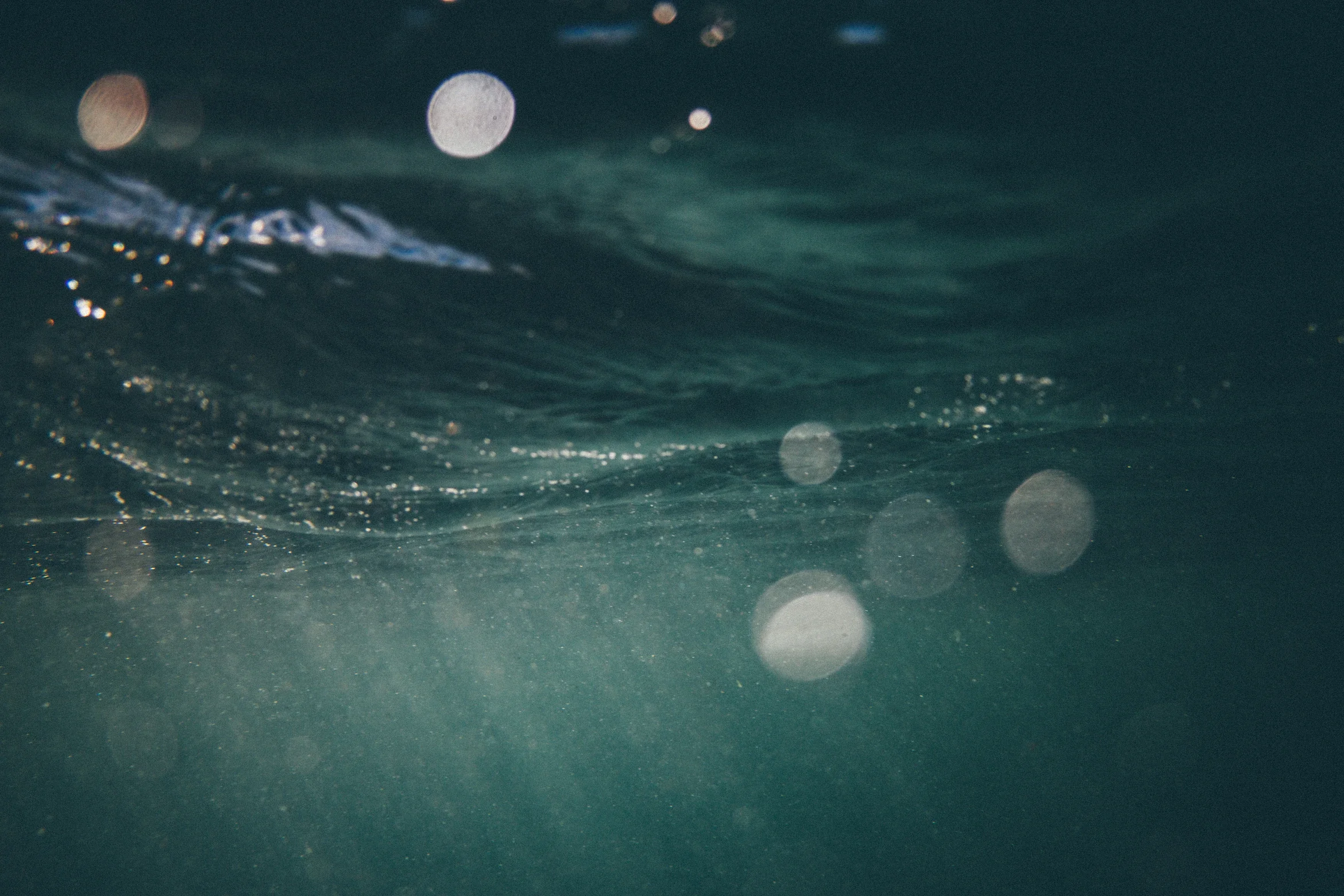 Underwater scene with bubbles and ripples on the water surface, dimly lit with a bluish-green tint.