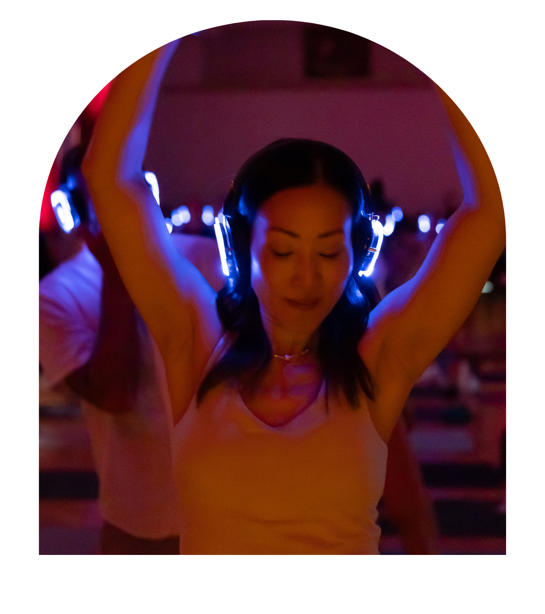 Catherine SoYoung, a young woman with dark hair wearing headphones and a light-colored tank top dancing with her eyes closed in a dimly lit room with colorful lights.
