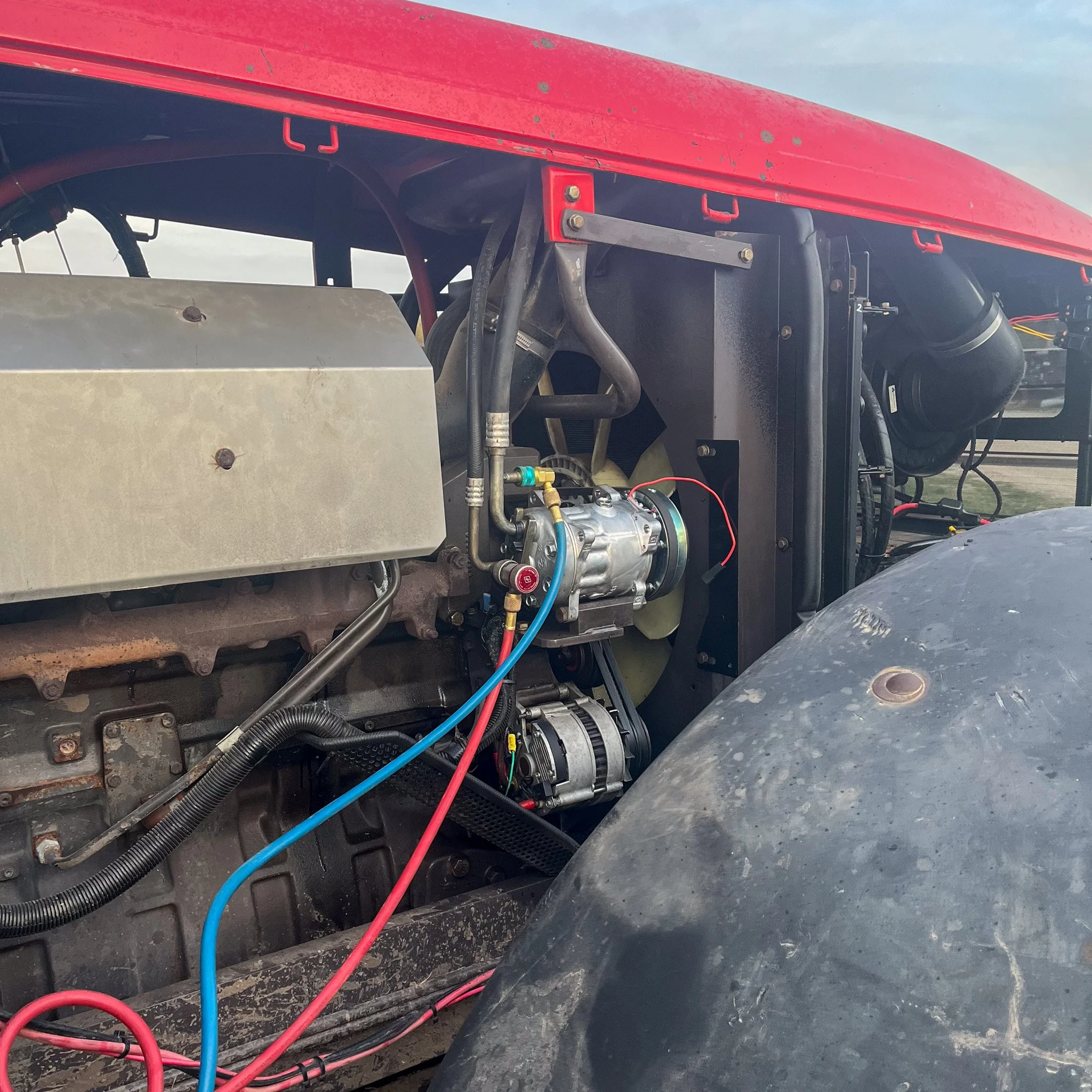 Close-up of a tractor's engine with various hoses, wires, and mechanical components visible, including a silver starter and black air intake pipe.