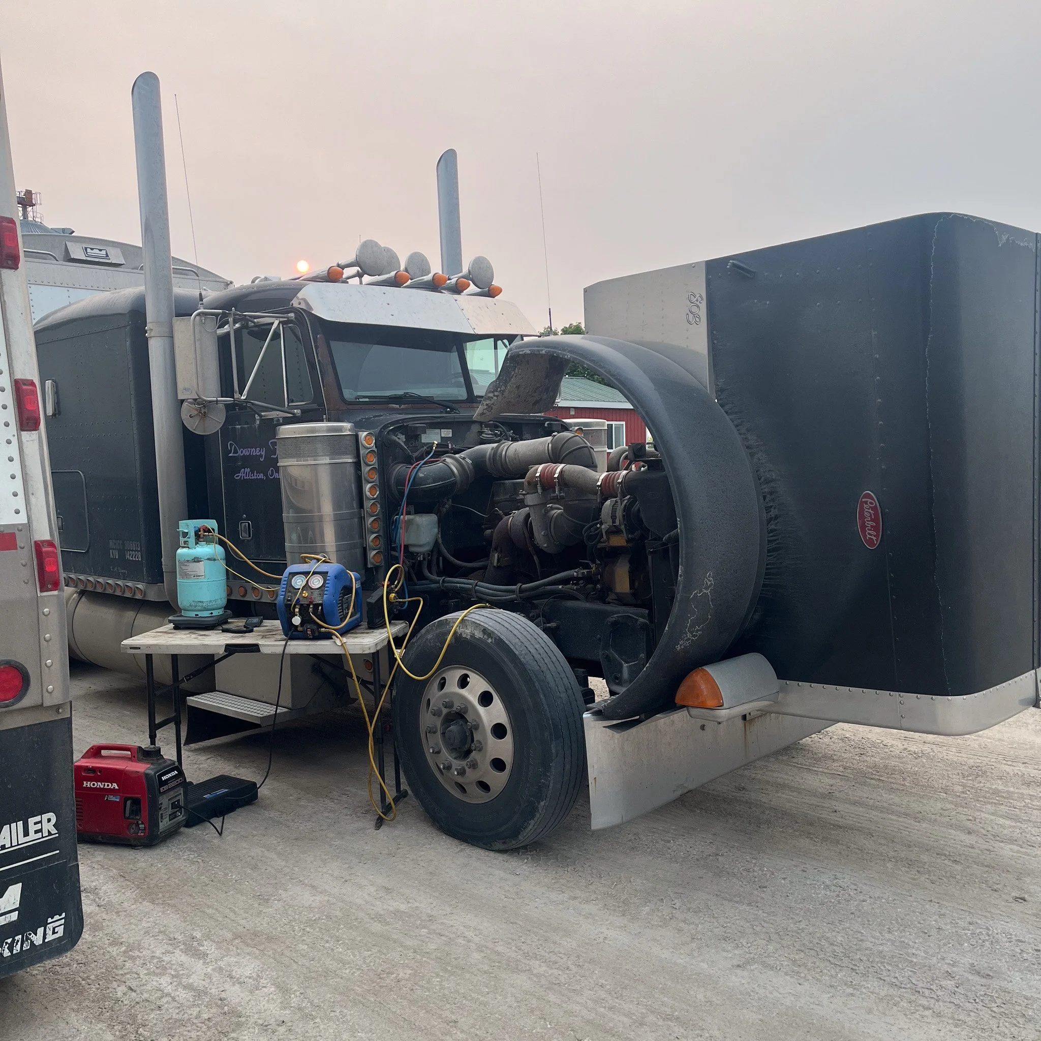 Semi-truck with its hood open, showing the engine being serviced with tools and equipment nearby on a table and ground.