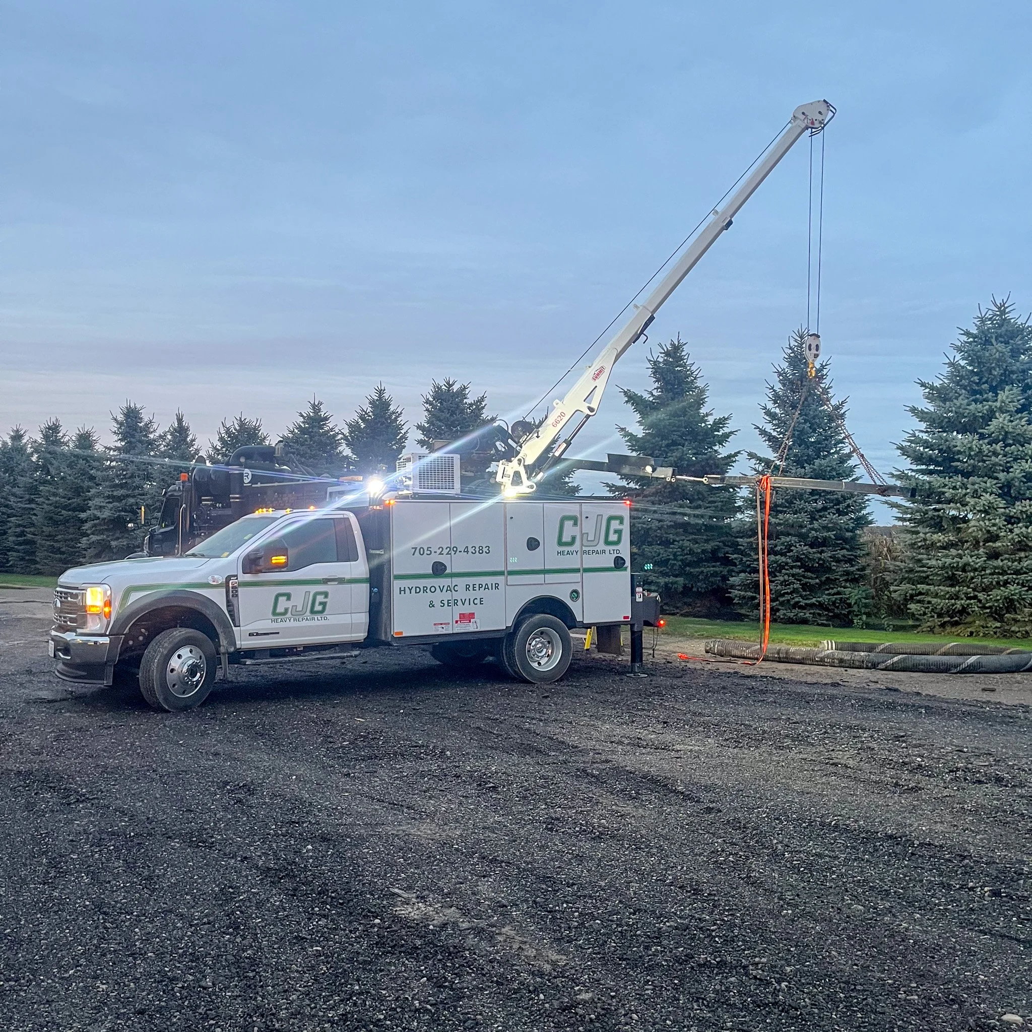A heavy-duty service truck with a crane arm is working on roadside tree trimming or maintenance in a parking lot. The truck belongs to C.J.G Heavy Repair Ltd.