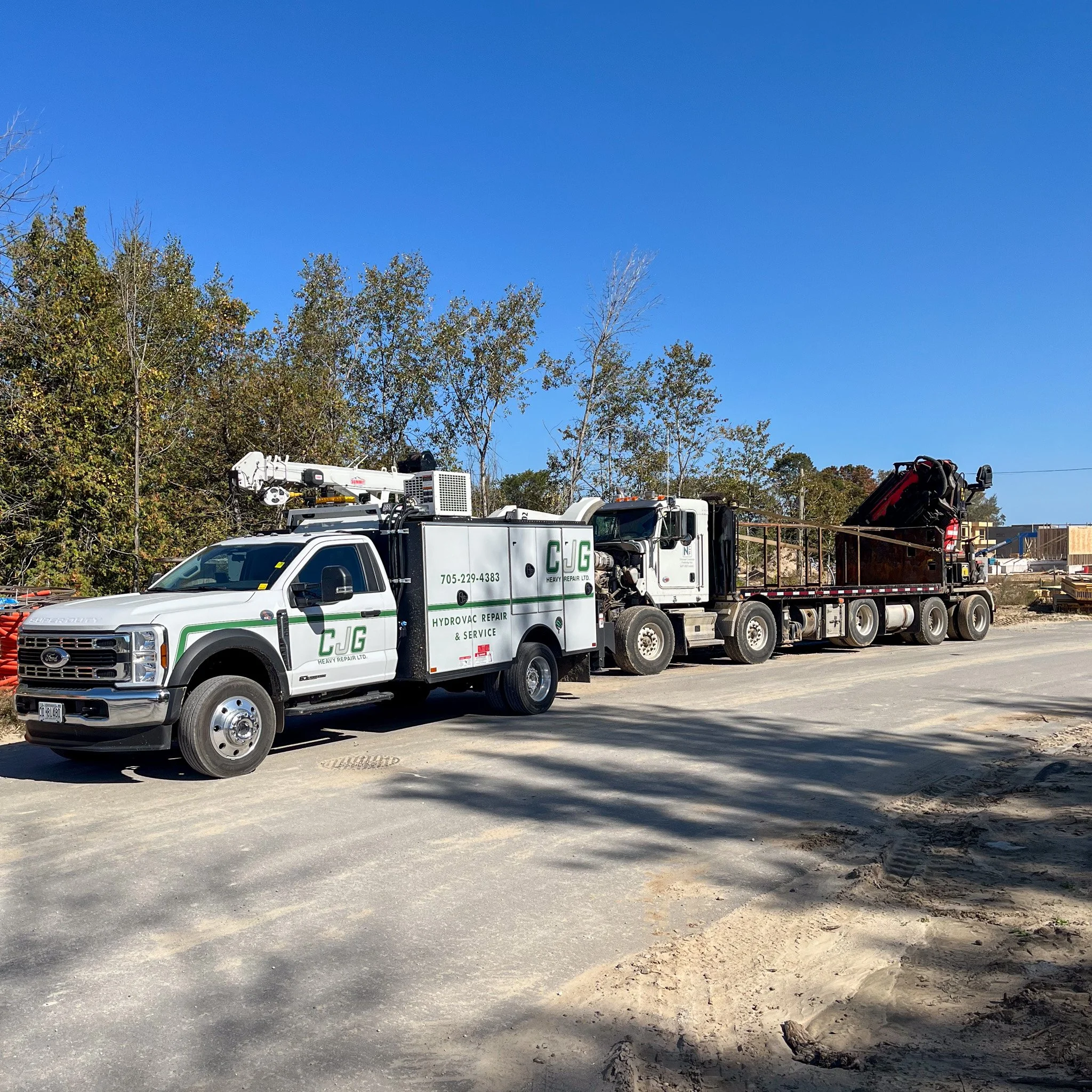 Utility truck with a crane at a construction site on a clear day with blue sky and trees in the background.