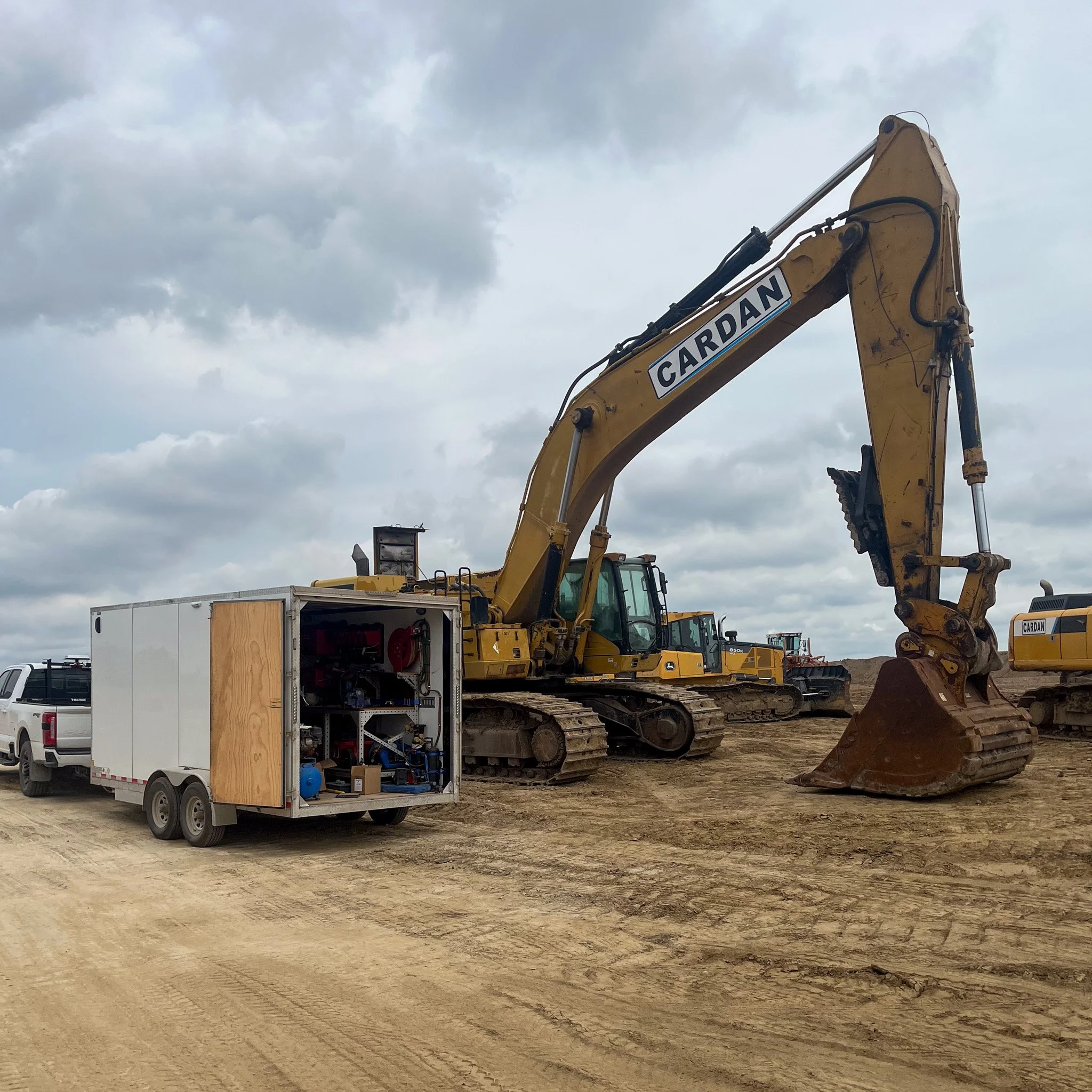 Construction site with a large yellow excavator labeled 'Cardan' and a white service trailer nearby, under a cloudy sky.