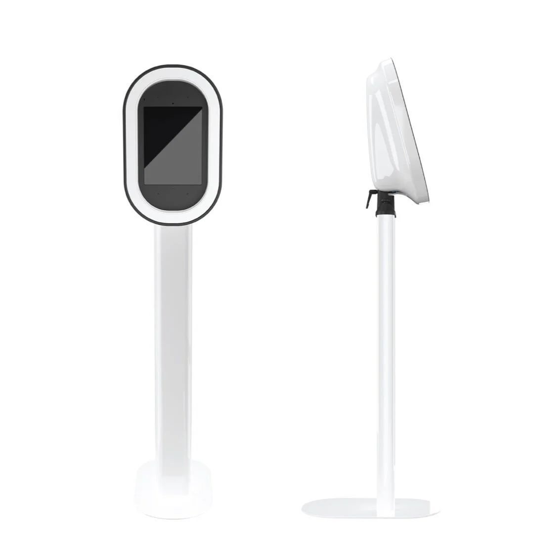 Front and side view of a modern, white, touchscreen kiosk with a vertical rectangular screen and an oval frame, mounted on a white stand.