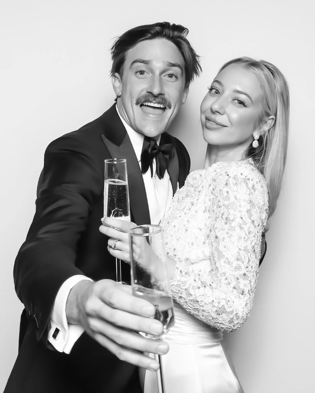 A black and white photo of a man and woman celebrating with champagne, both smiling, with the man holding two glasses of champagne.