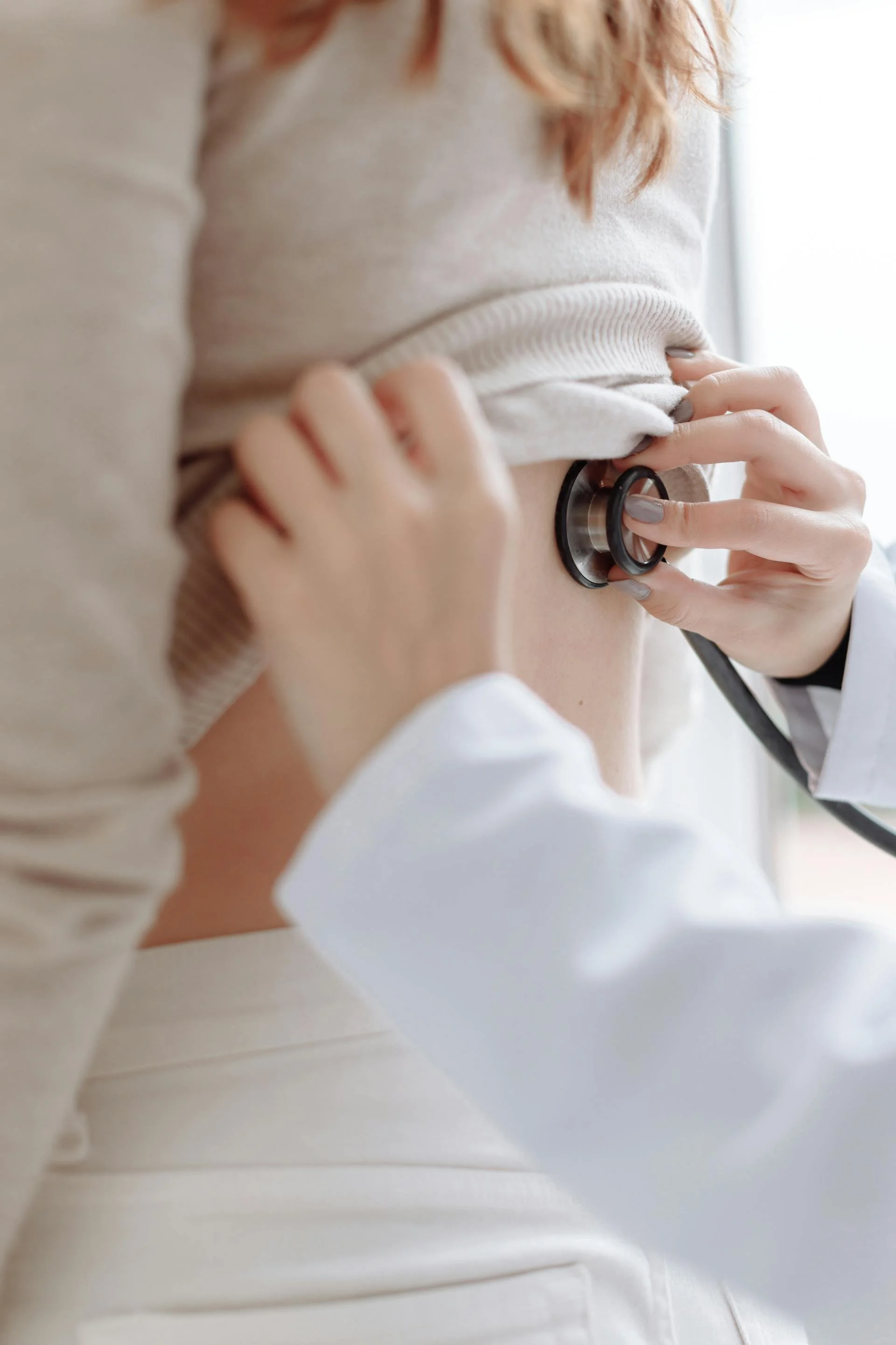 A healthcare professional using a stethoscope on a woman's side during a medical examination.