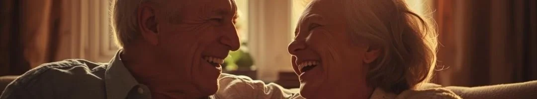 An elderly man and woman are smiling and laughing together indoors.