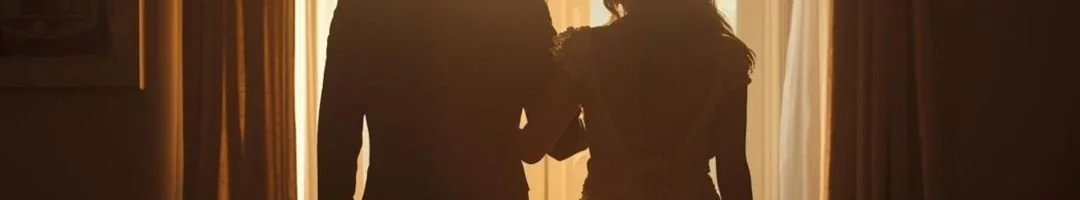 Two women standing near a window with curtains, backlit by sunlight, holding hands.