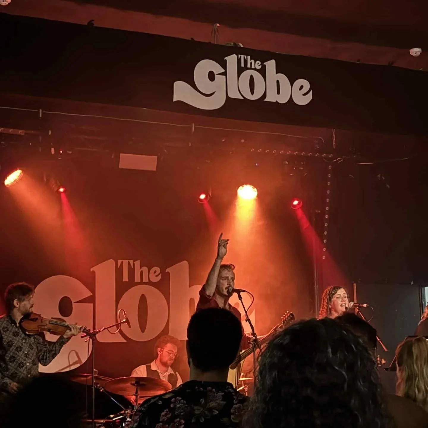 A live musical performance at The Globe, with musicians on stage under red and orange lights, and the venue's sign visible overhead.