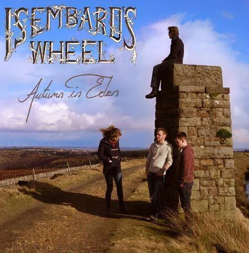 Three people standing on a dirt path near a stone monument with a seated statue on top, overlooking a rural landscape under a partly cloudy sky.