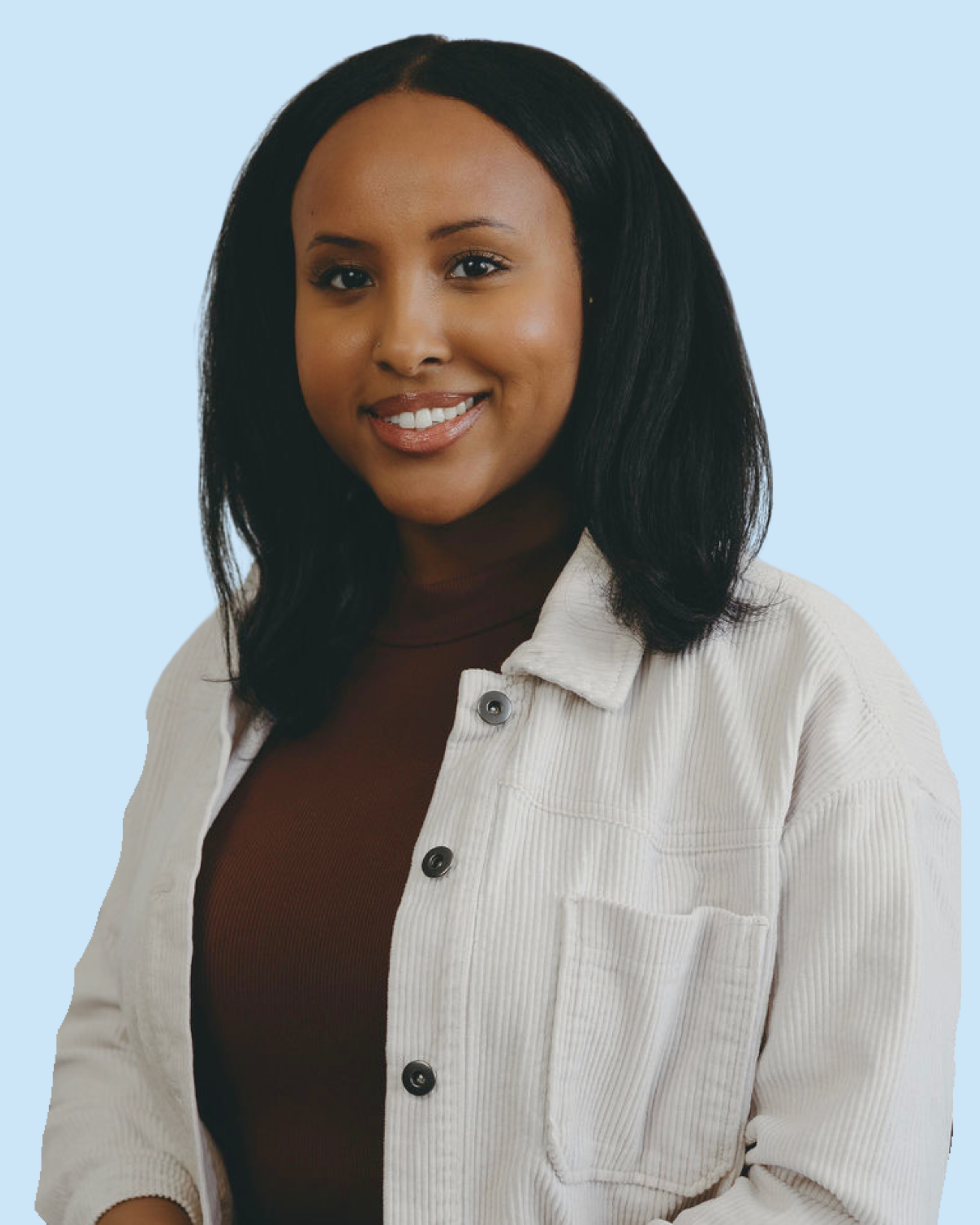 Portrait of a young woman with black hair, smiling, wearing a white jacket over a brown shirt, against a light blue background.