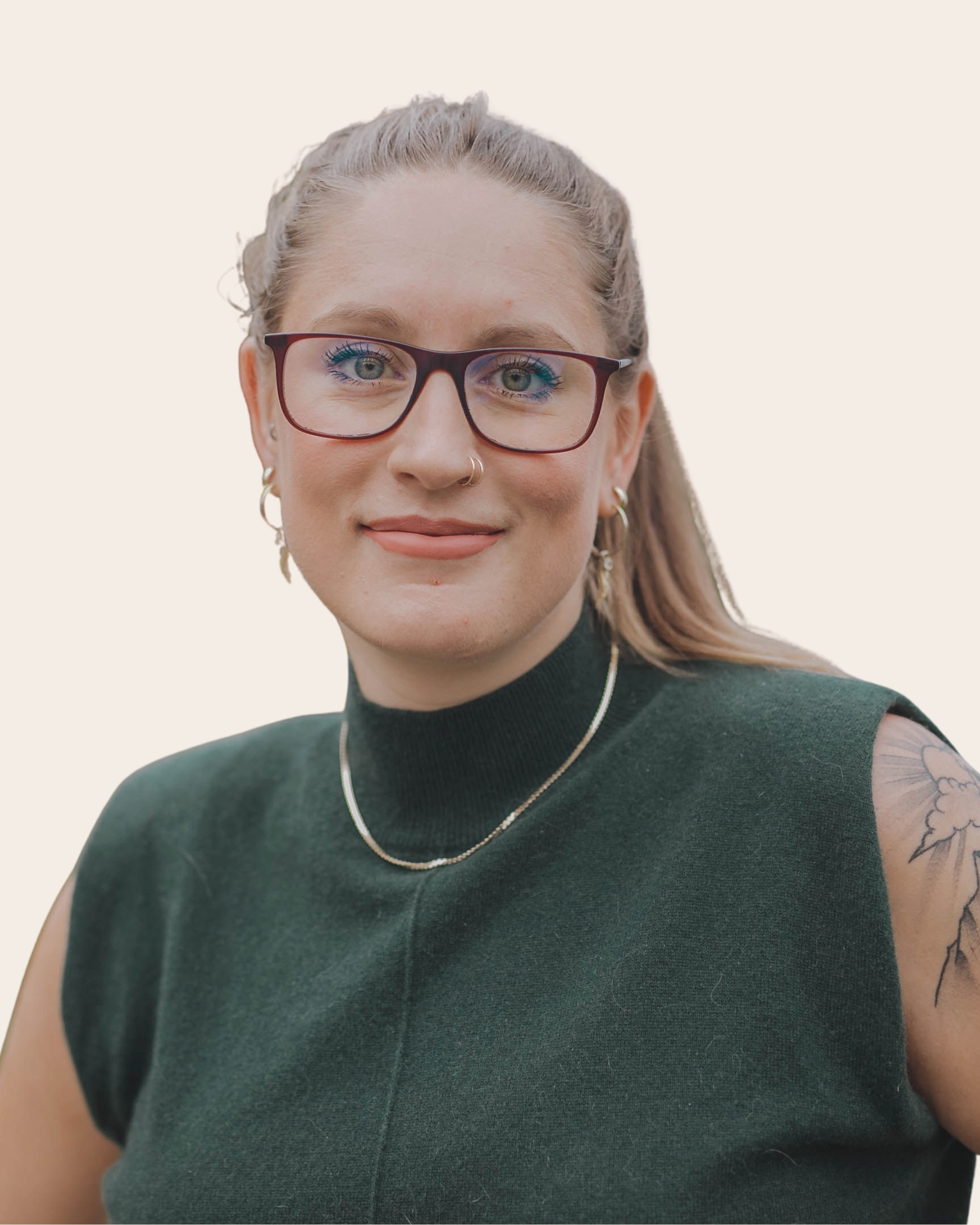 A young woman with blonde hair, wearing glasses, earrings, a nose ring, and a necklace, smiling outdoors against a neutral background.