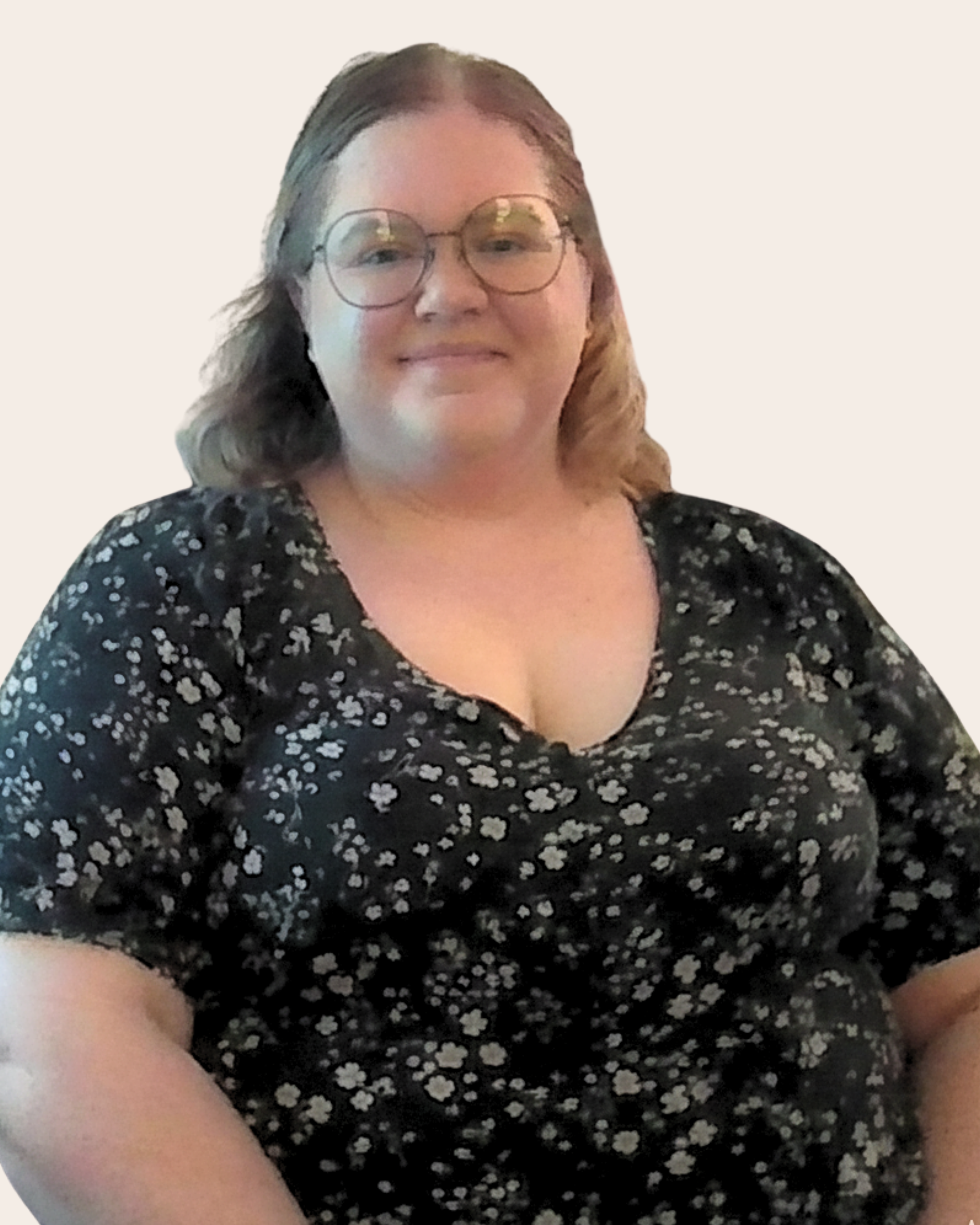 A woman with glasses and shoulder-length wavy hair, smiling, wearing a black dress with white floral pattern, sitting against a plain light background.