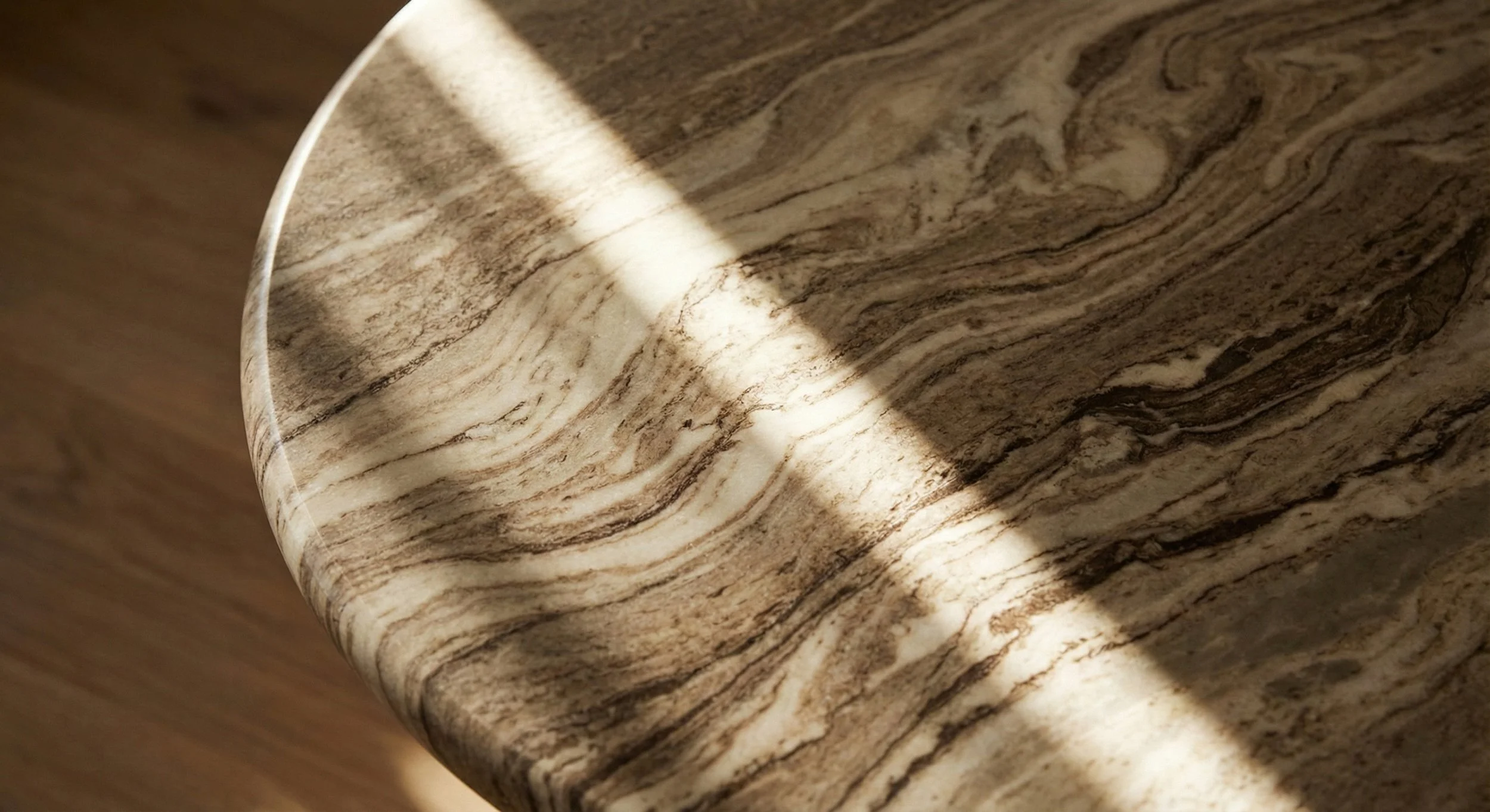 Close-up of a round marble table with brown and beige swirling patterns, with sunlight casting a shadow on it.