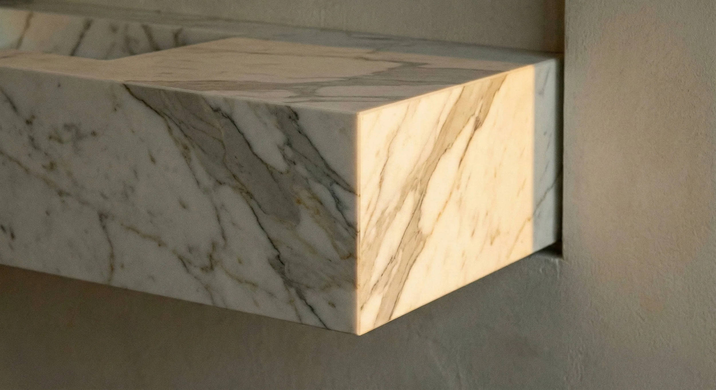 Close-up of a marble wall ledge with white and gray veining, mounted on a beige wall.