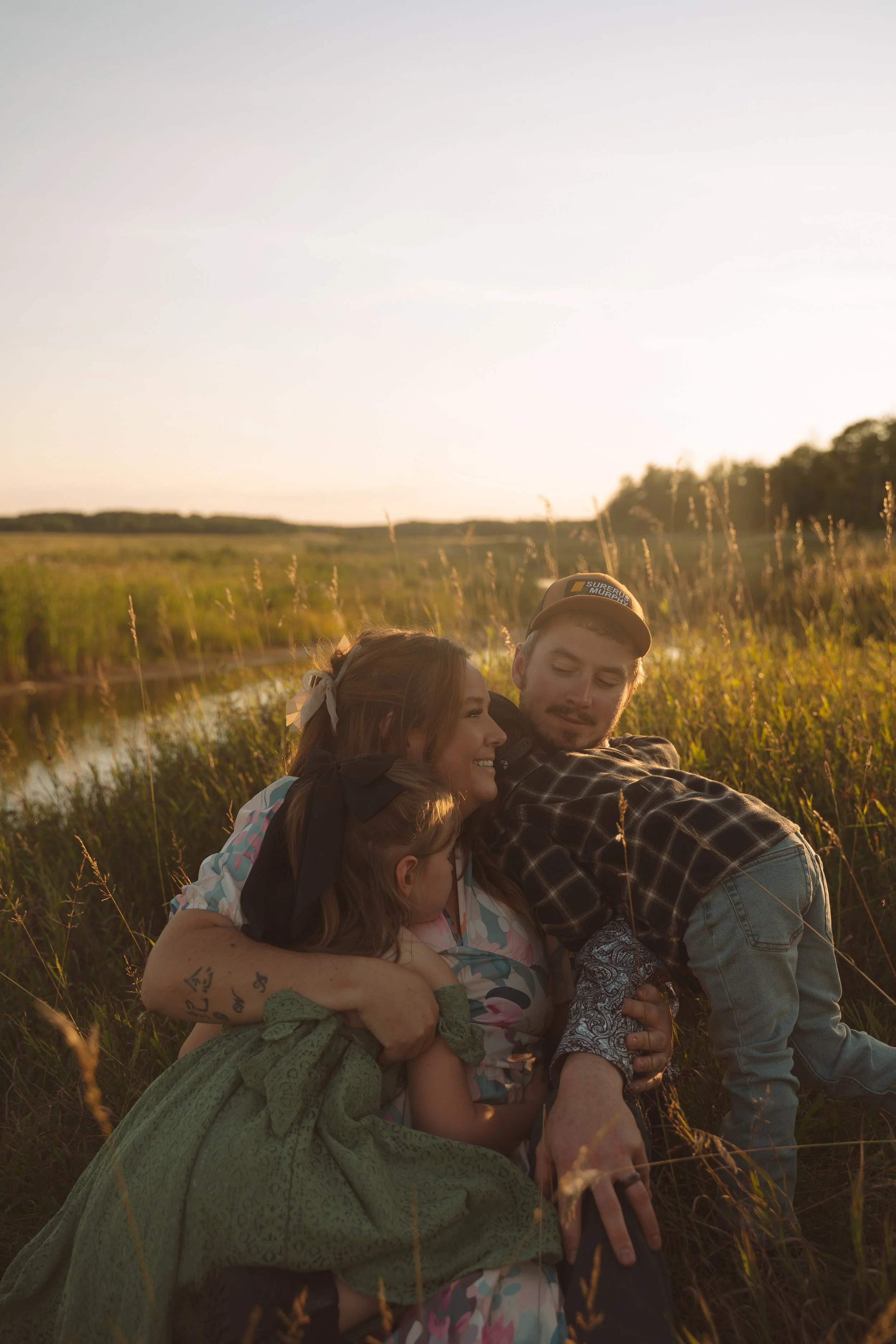 A family of four enjoying sunlight together outdoors in a field of tall grasses, near a small water body.