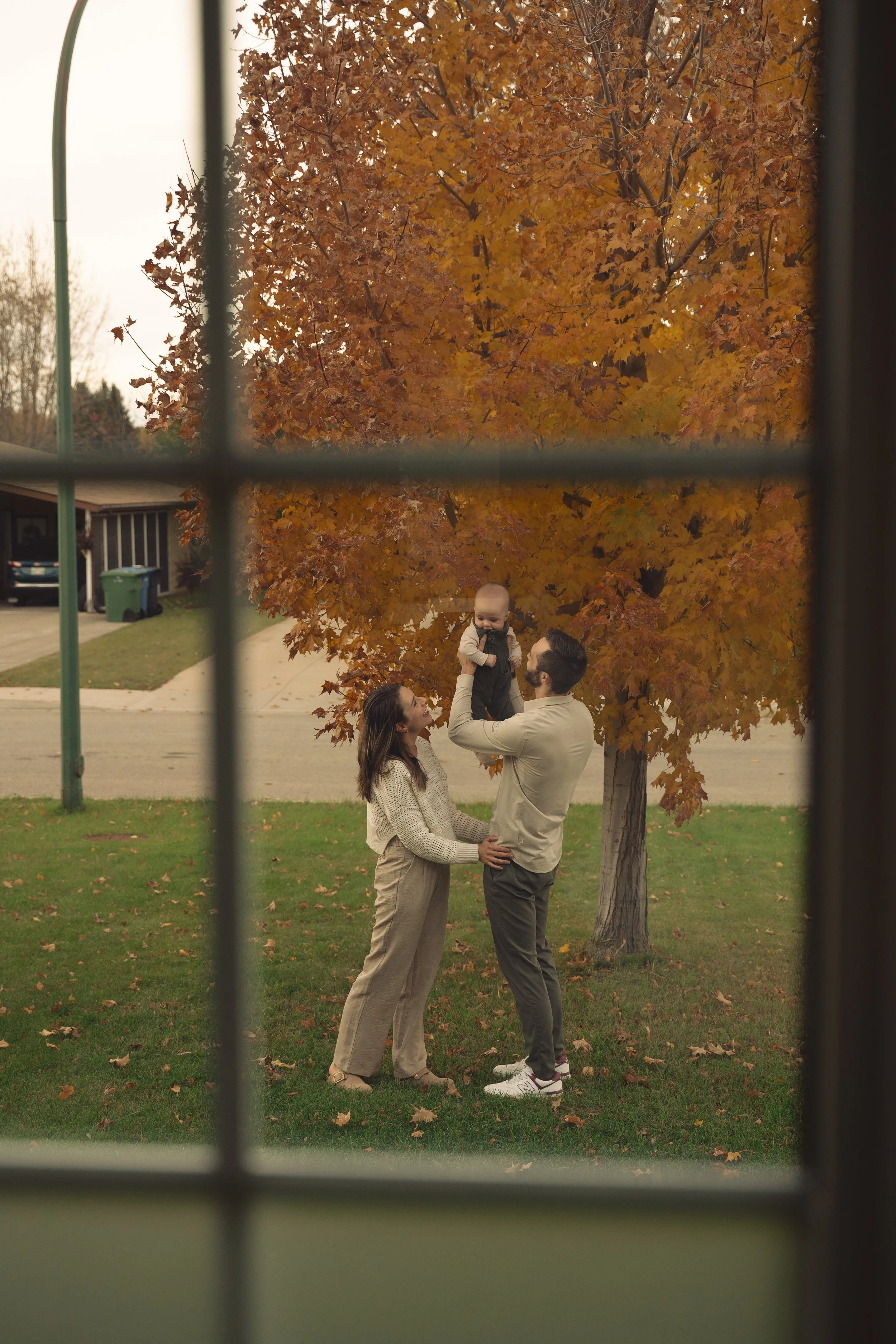 Family standing outdoors during fall, with a large orange tree in the background, viewed through a window.