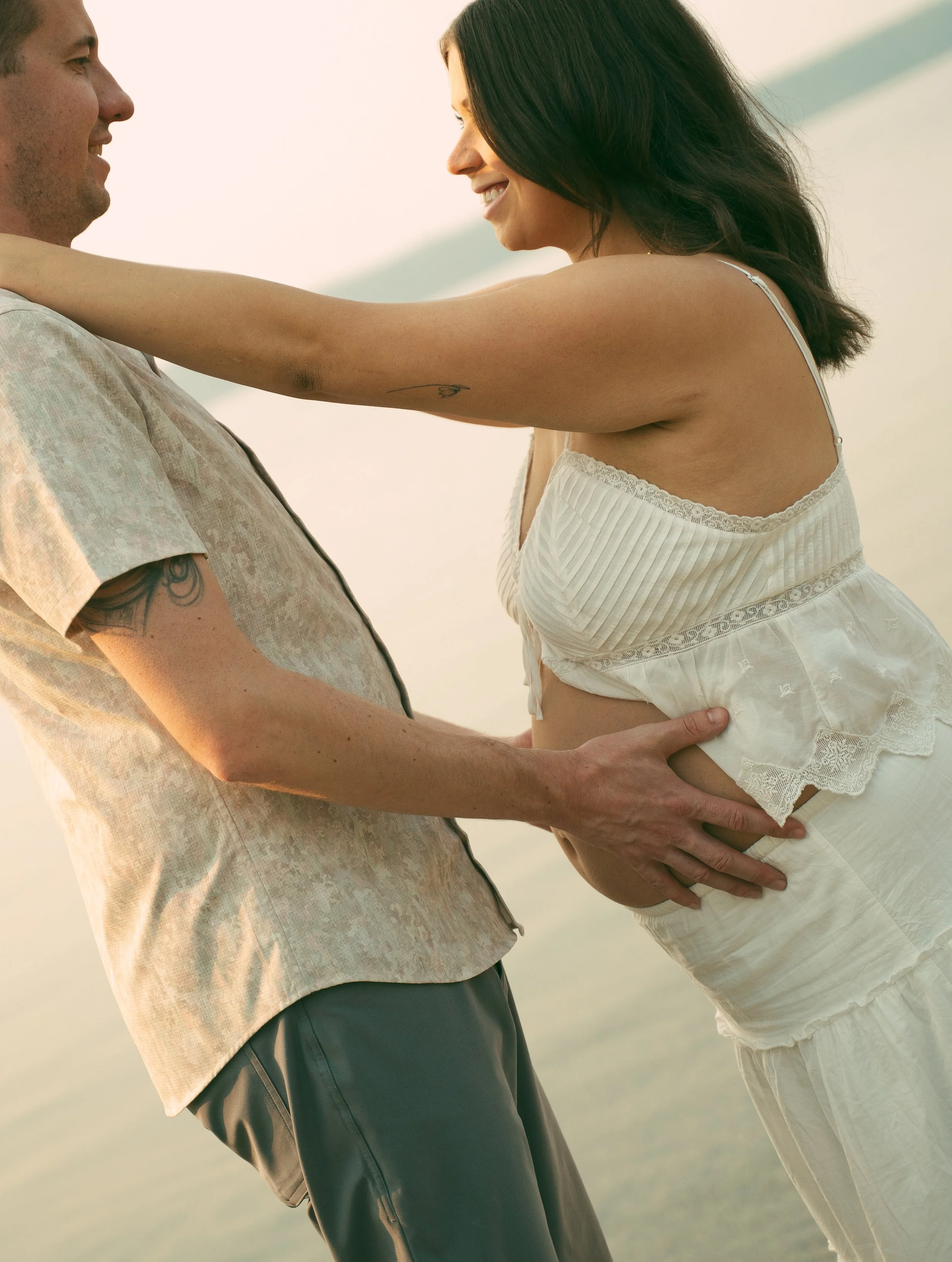 A couple standing on a beach, embracing each other with a sunset in the background.