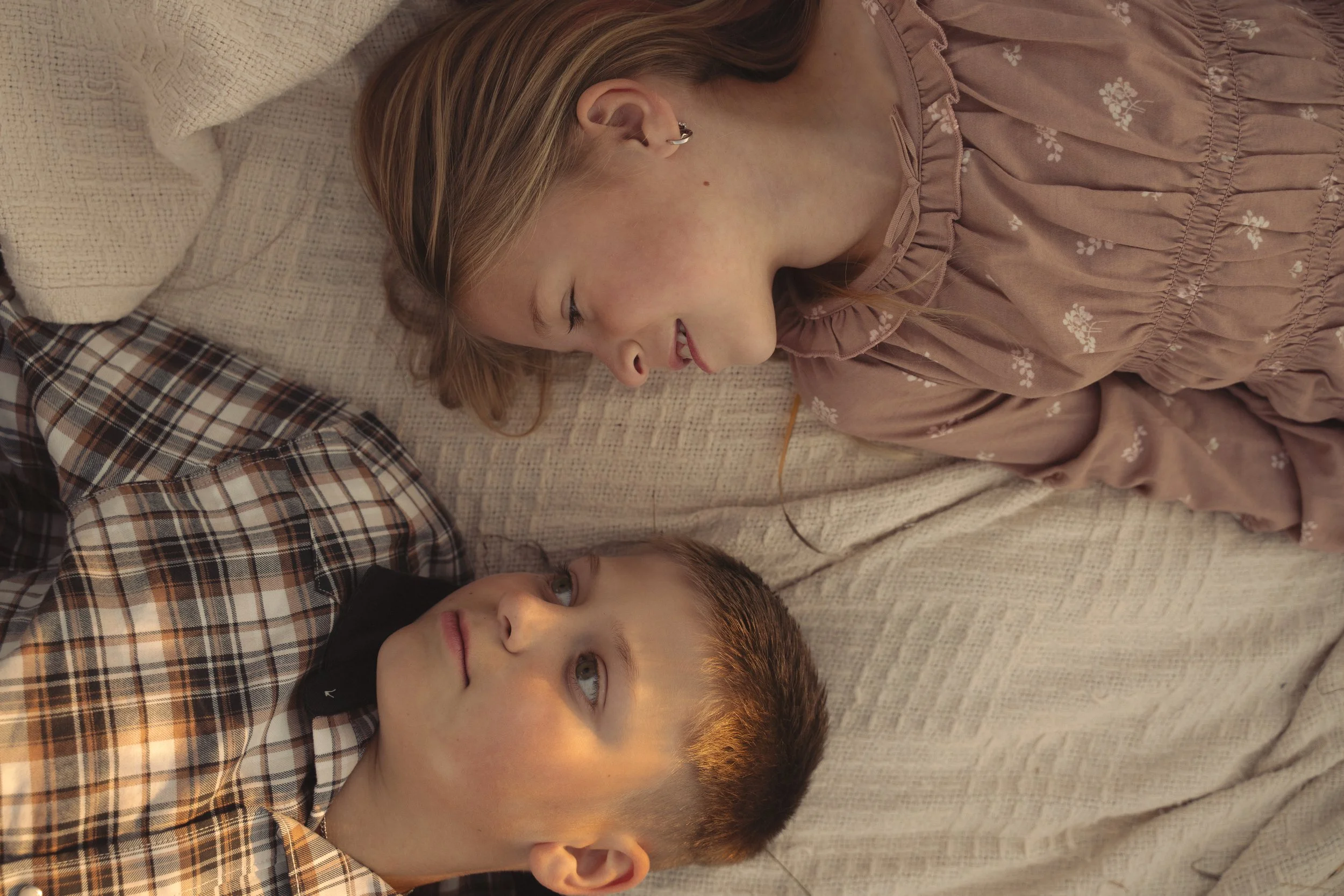 A young woman and a young boy lying on a beige couch, looking at each other and smiling.