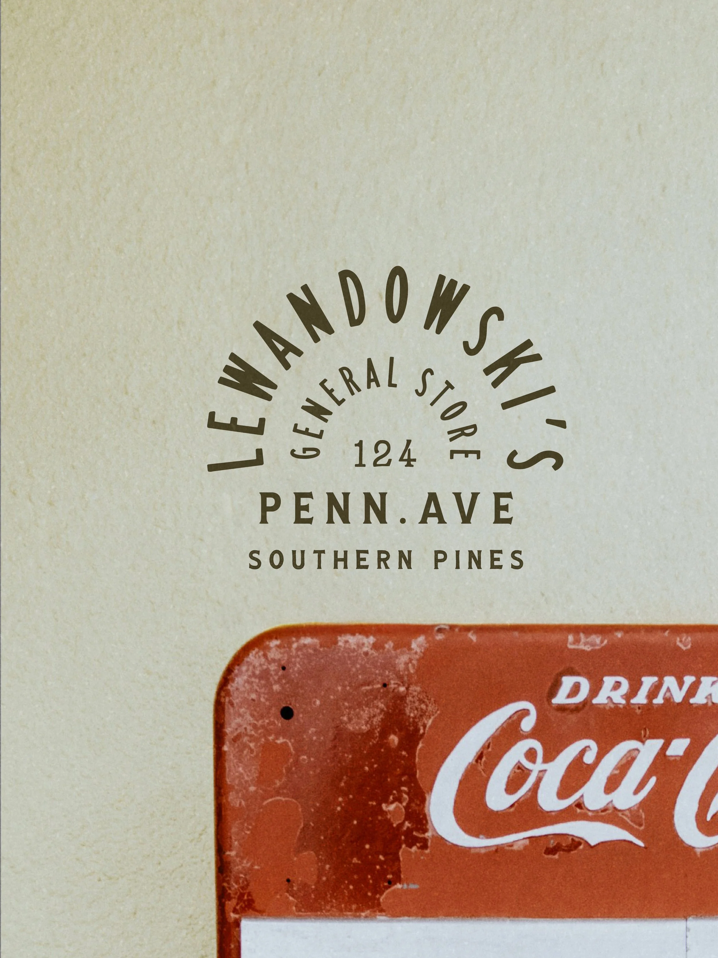 Close-up of vintage sign with text: 'Lewandoski's General Store, 124 Penn Ave, Southern Pines' and part of a red Coca-Cola sign at the bottom.