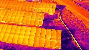 Aerial drone thermal inspection of commercial municipal solar installation showing damaged and malfunctioning solar panels in need of urgent repair or replacement.