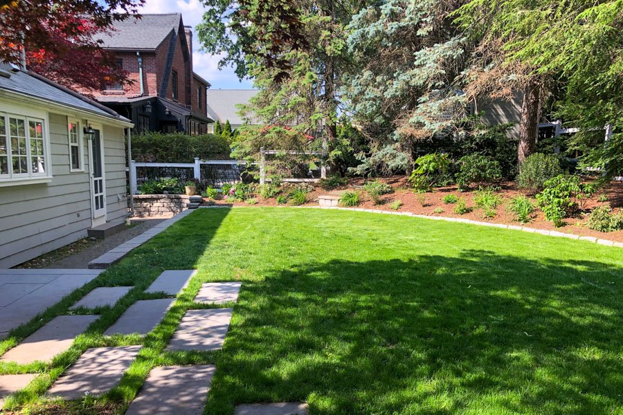  Outdoor couch and chairs on irregular stone patio with planting bed and lawn 