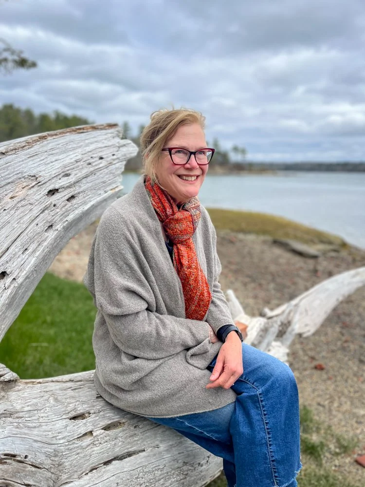 Elizabeth Gourley sitting on a piece of driftwood on the coast of Maine.