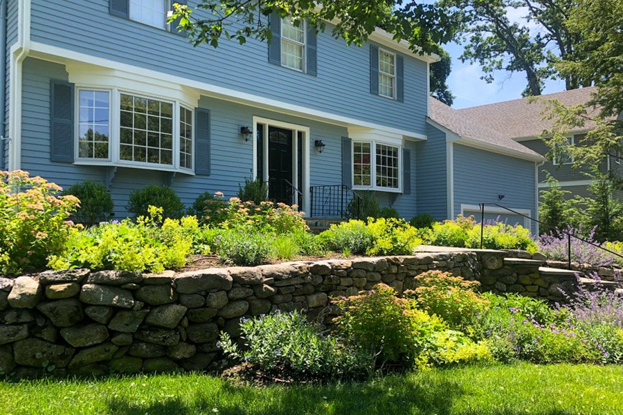  Rebuilt stone retaining wall with blooming shrubs and perennials at top and bottom 