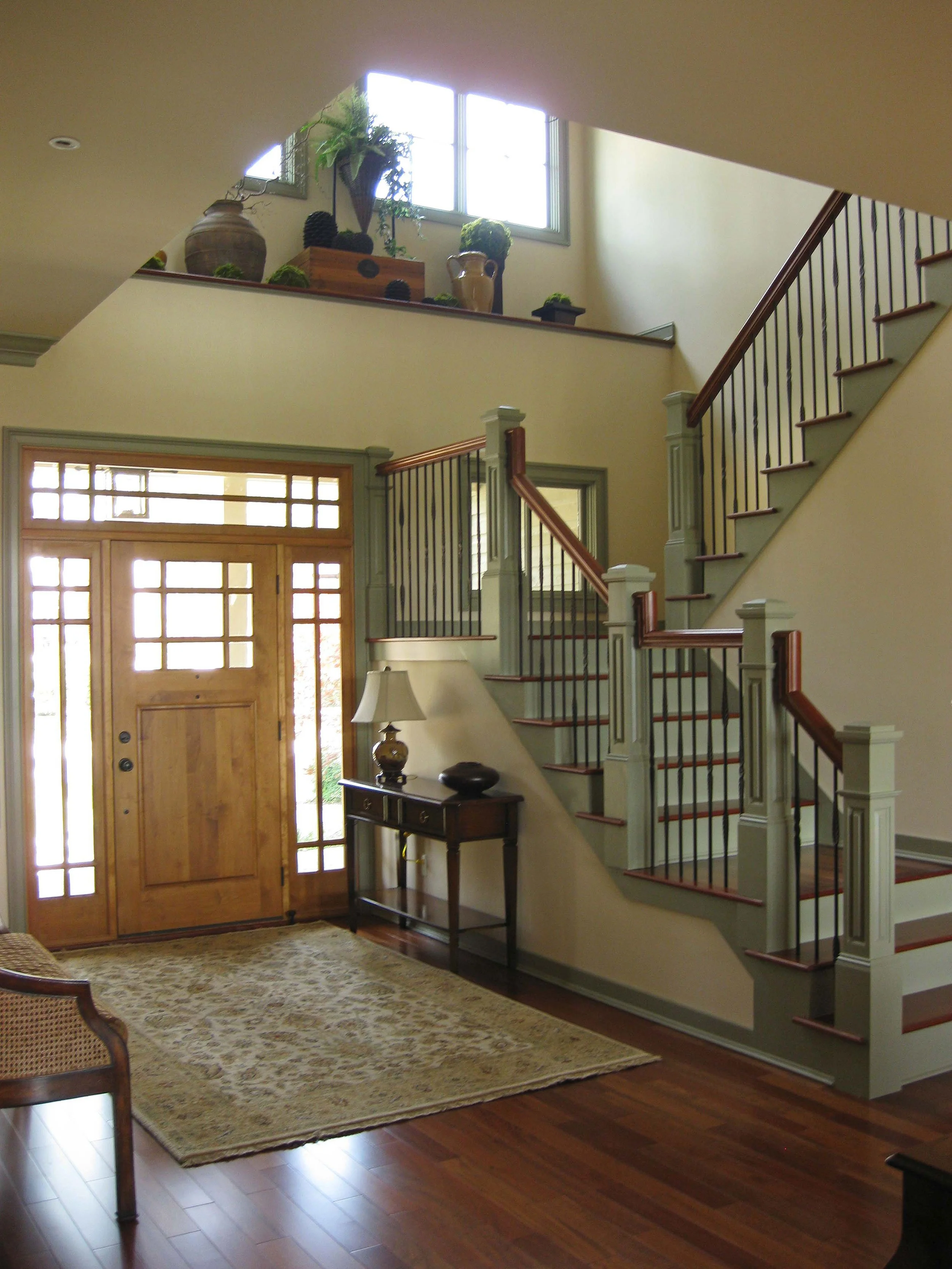 Entryway with wooden front door and a staircase leading up to the second floor, decorated with plants and a rug on the hardwood floor.