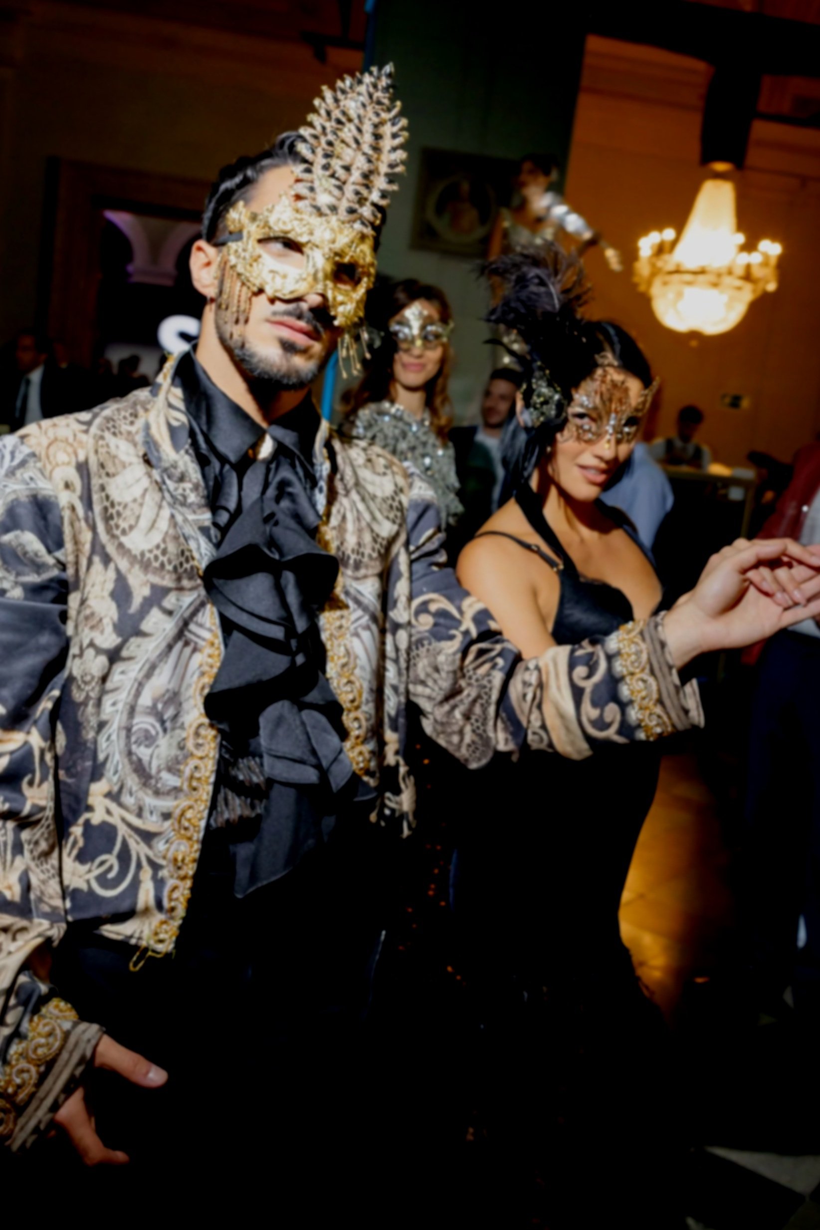 Three people dressed in ornate, masks, and costumes at a fancy event or masquerade ball.