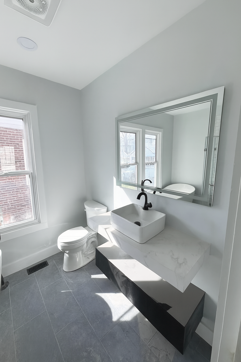 Modern bathroom with a white toilet, a marble vanity with a vessel sink and black faucet, and large windows letting in natural light.