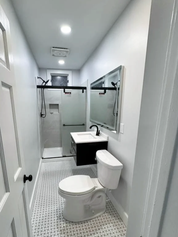 Small bathroom with a shower, toilet, sink with mirror, and black accents.