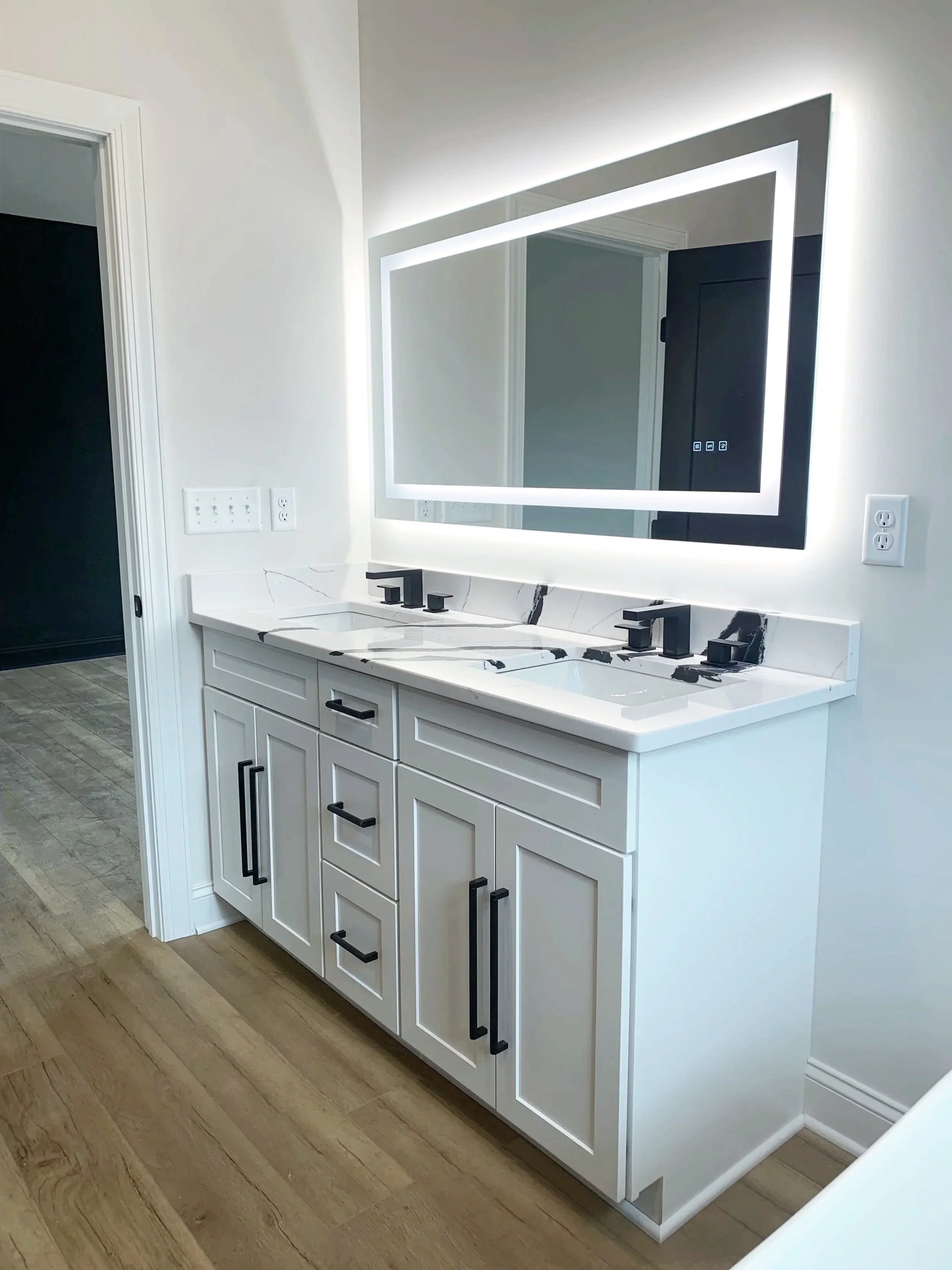 Modern white bathroom vanity with black hardware, two sinks with black fixtures, mirror with LED lighting, and a white marble countertop, in a contemporary bathroom.