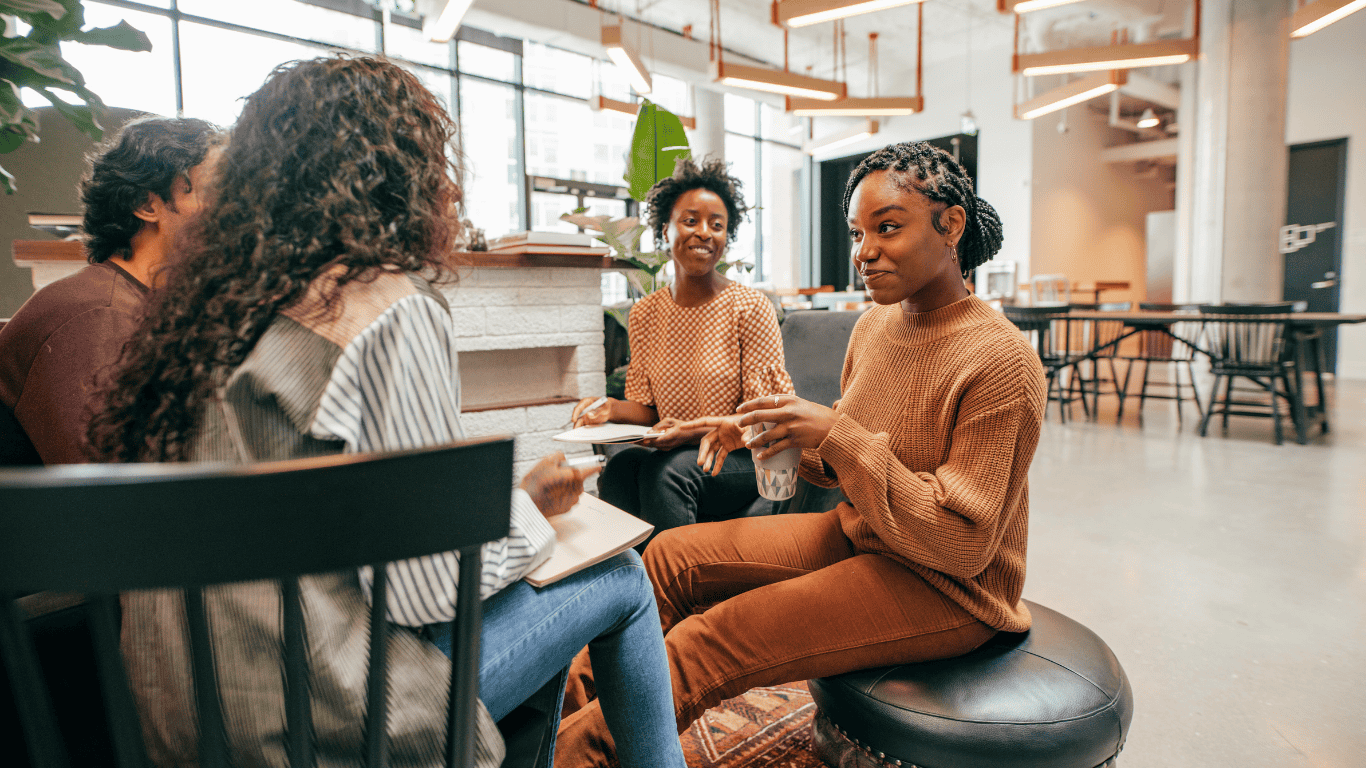 Business meeting with four professionals sitting around a table, with laptops and documents, in a modern office setting.