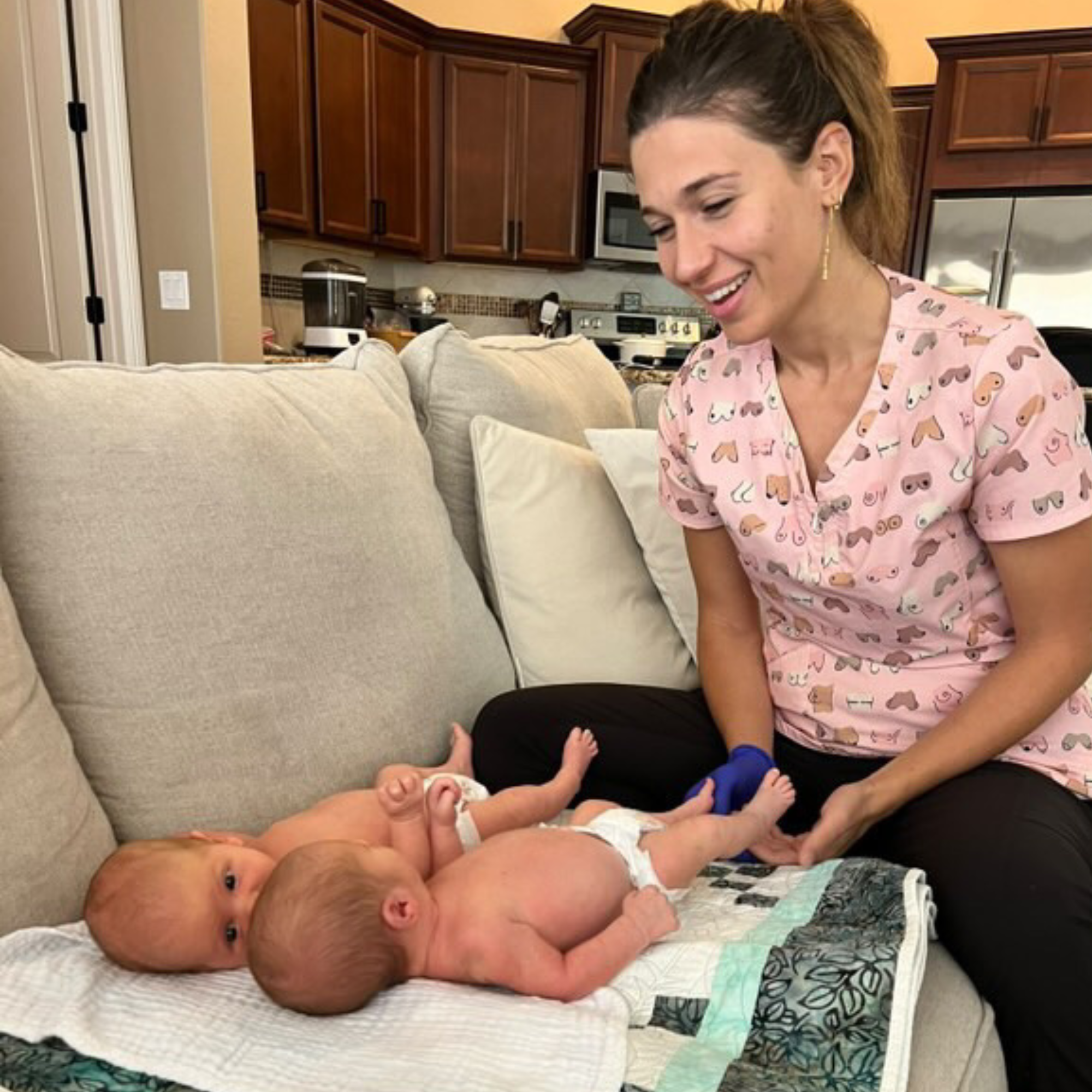 Caregiver smiling while guiding two newborn babies during tummy time on a couch, supporting early development, bonding, and infant movement exercises in a home setting