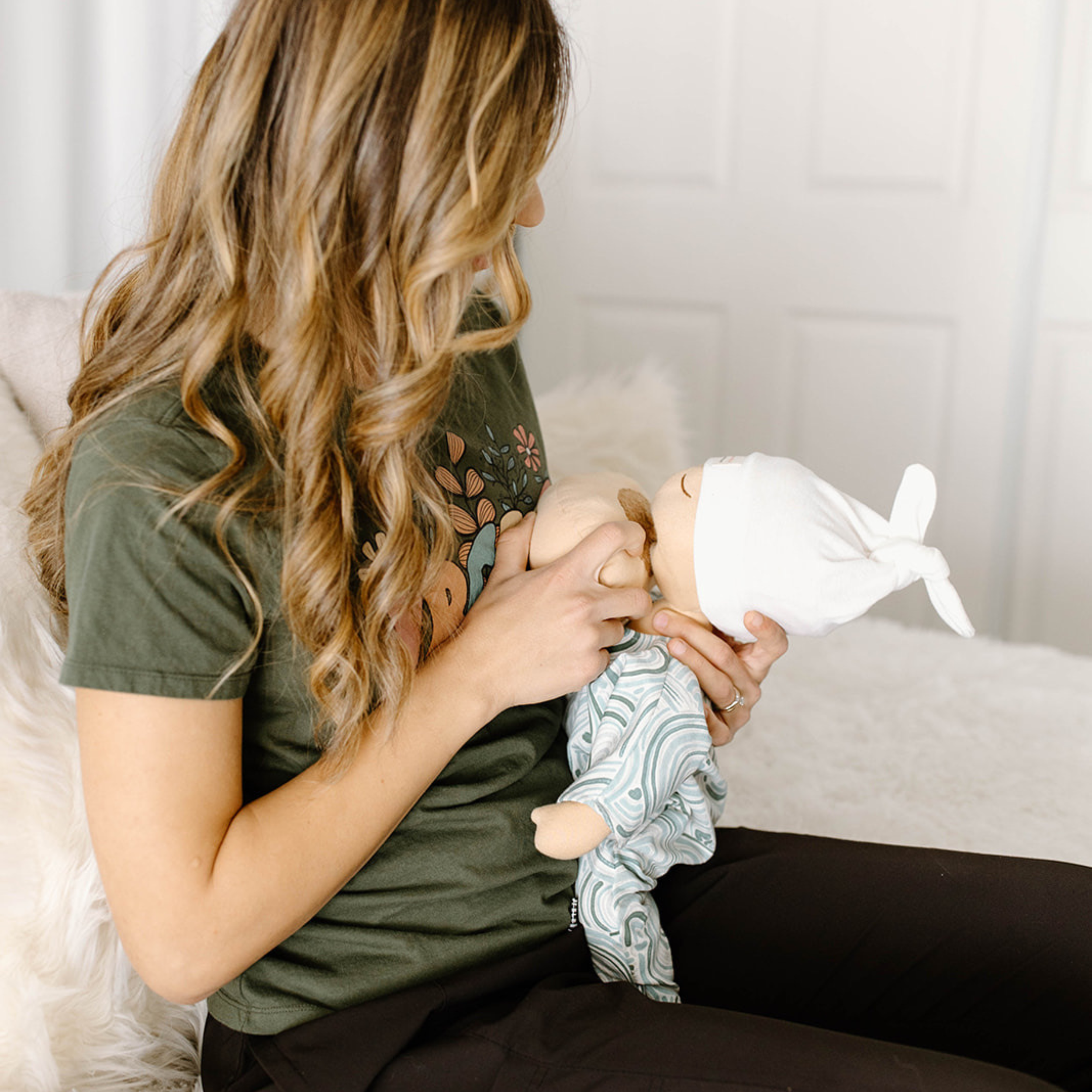 Lactation consultant demonstrating breastfeeding positioning with a baby doll, providing hands-on feeding education, latch guidance, and newborn care instruction